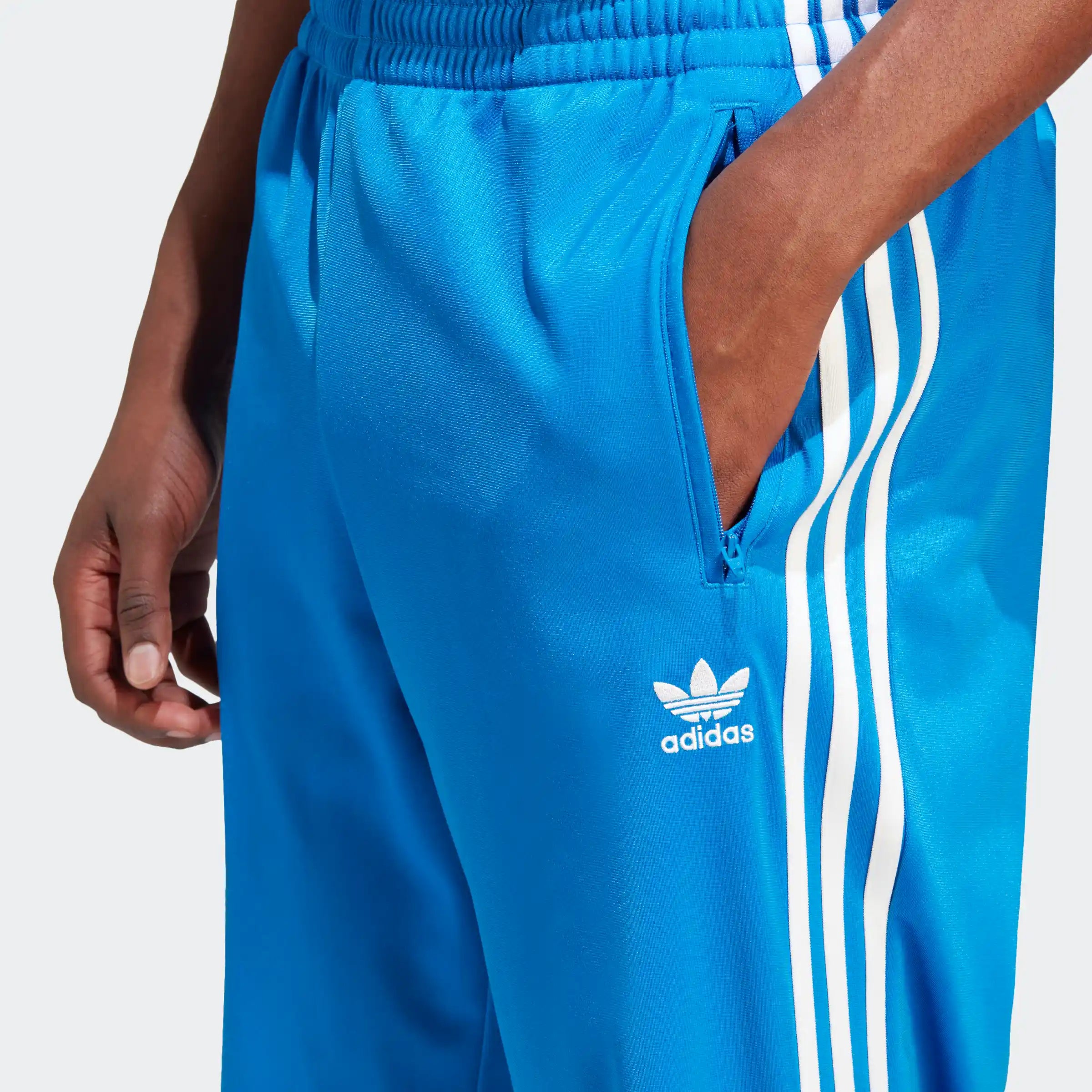 „Blaue Adidas-Trainingshose mit weißen Seitenstreifen und kleinem Logo links.“