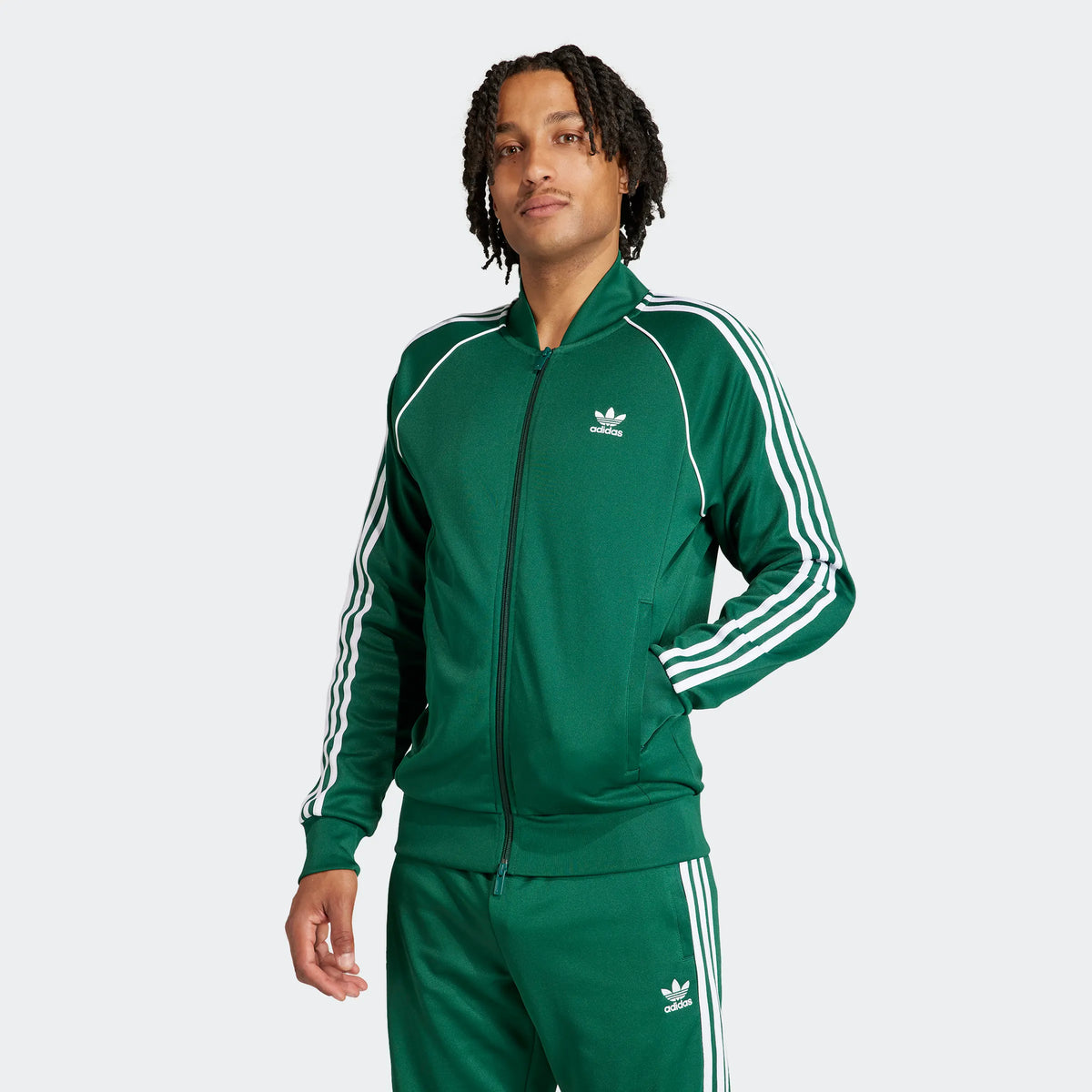 Herren-Model trägt eine grüne adidas Originals SST Trainingsjacke mit weißen 3-Streifen und Trefoil-Logo vor dem STICKABUSH Store in Berlin-Kreuzberg.