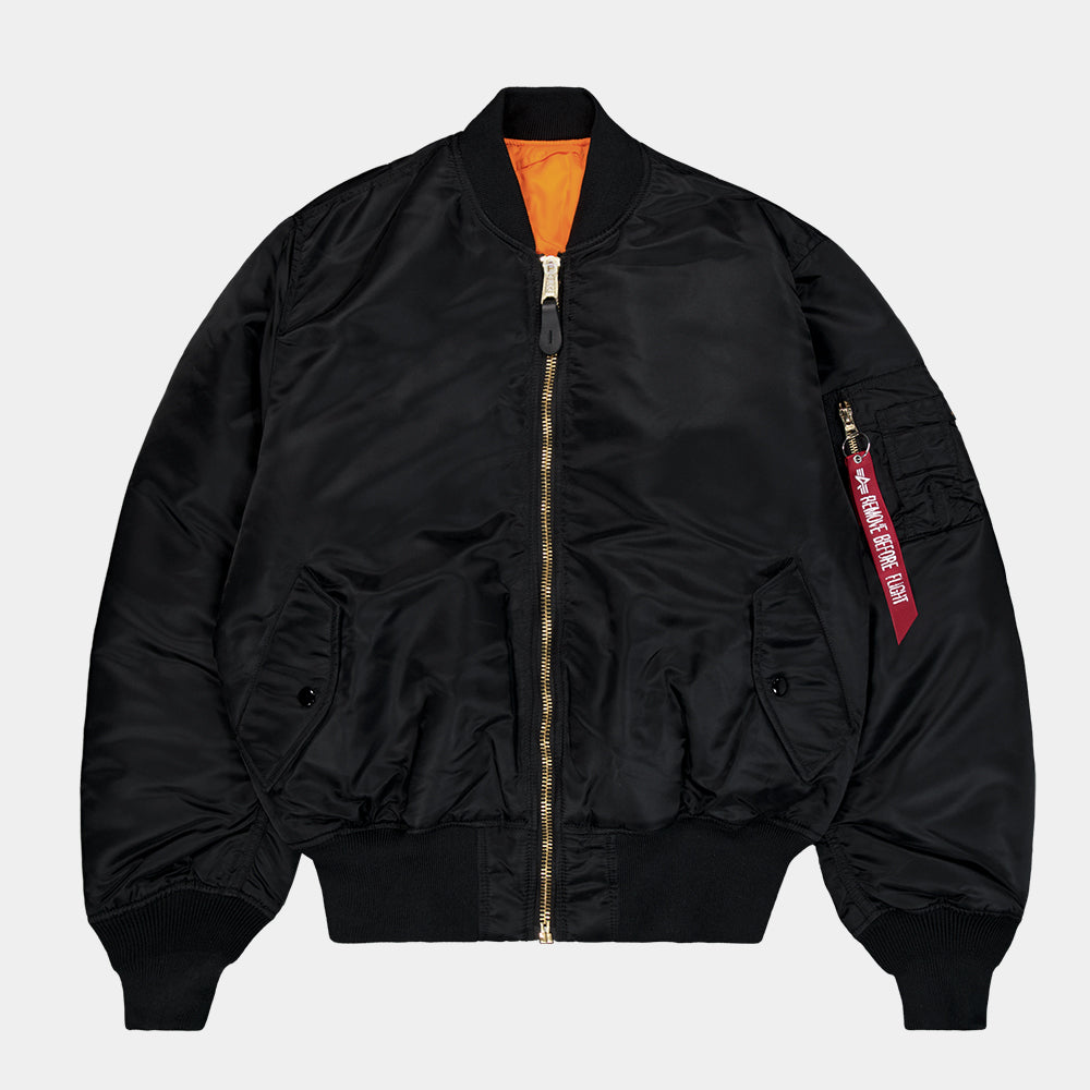“Alpha Industries MA-1 (HERITAGE) Bomberjacke in Schwarz, aus robustem Nylon, mit ikonischem Flight-Tag am Ärmel und gestepptem orangenem Innenfutter.“