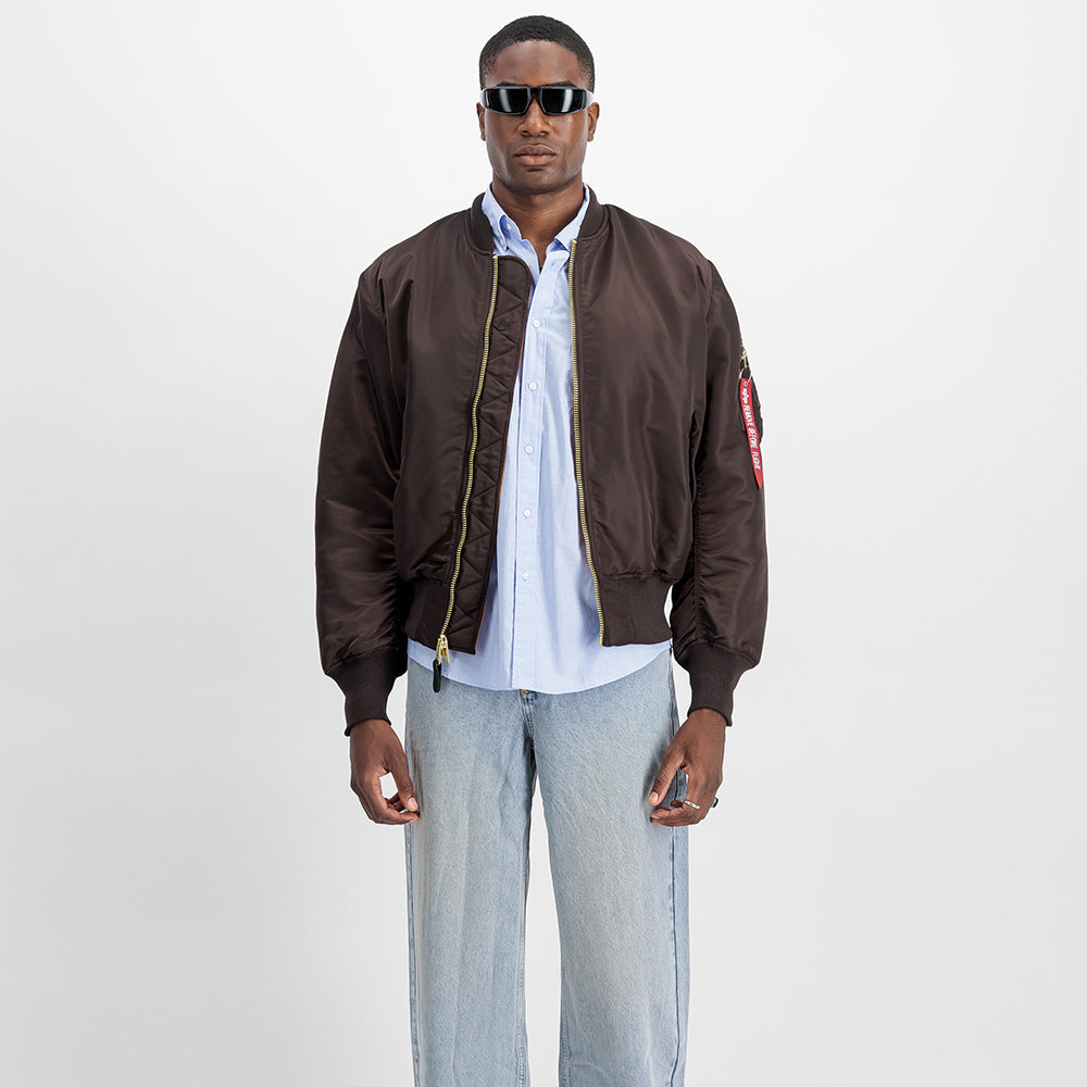 "Alpha Industries MA-1 (HERITAGE) Bomberjacke in Hunter Brown, aus strapazierfähigem Nylon, mit Rippbündchen und ikonischem Flight-Tag am Ärmel."
