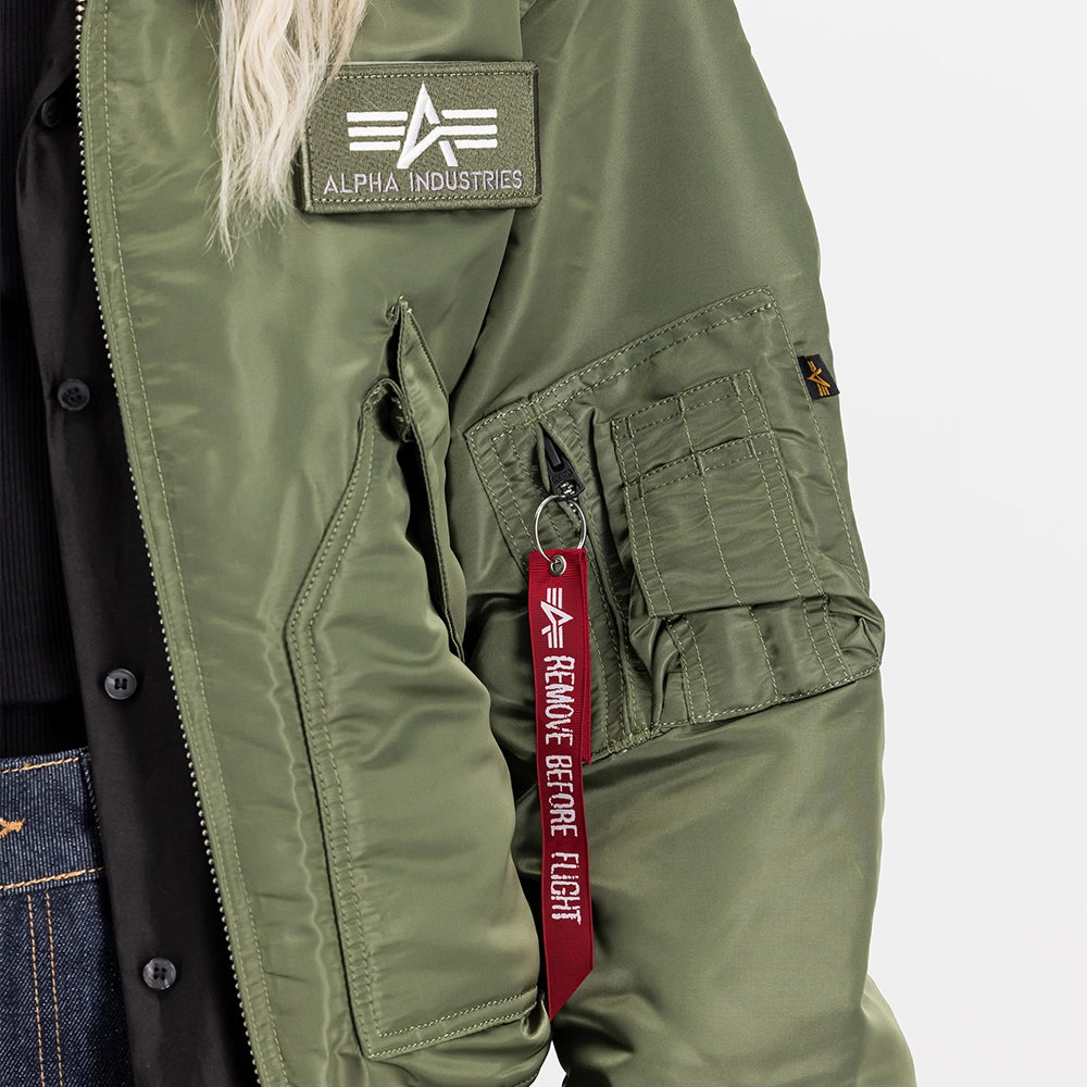 „Alpha Industries CWU 45 Heritage Bomberjacke in Sage Green mit Umlegekragen, Klettverschluss-Taschen und rotem Remove Before Flight Tag bei Stickabush Berlin.“