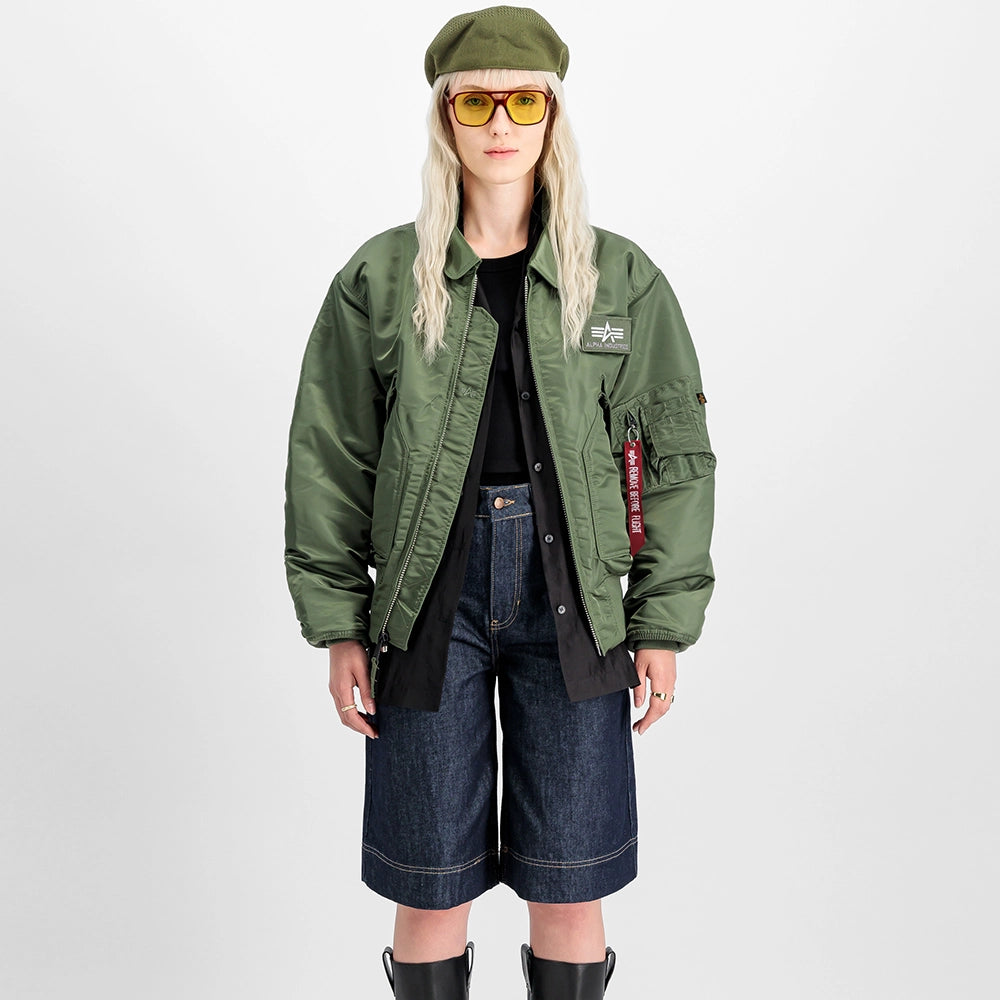 „Alpha Industries CWU 45 Heritage Bomberjacke in Sage Green mit Umlegekragen, Klettverschluss-Taschen und rotem Remove Before Flight Tag bei Stickabush Berlin.“