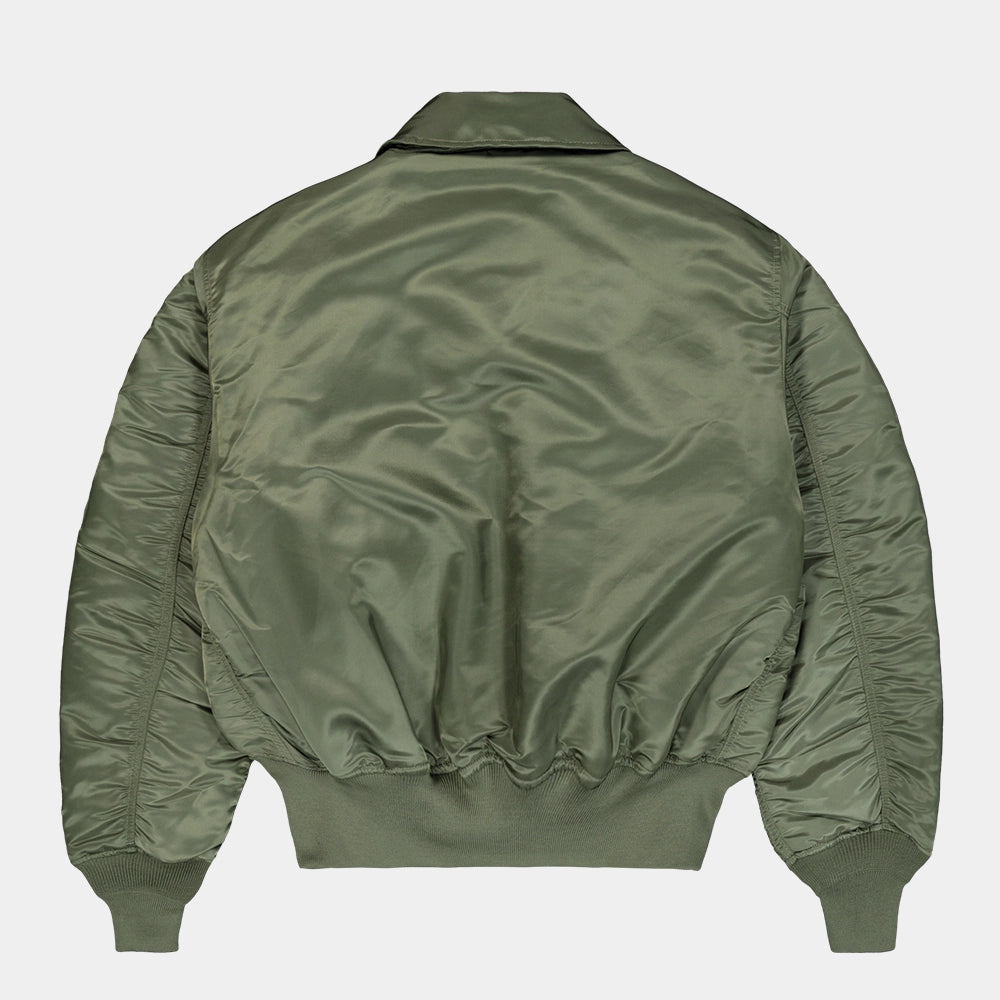 „Alpha Industries CWU 45 Heritage Bomberjacke in Sage Green mit Umlegekragen, Klettverschluss-Taschen und rotem Remove Before Flight Tag bei Stickabush Berlin.“