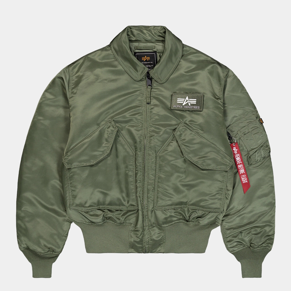 „Alpha Industries CWU 45 Heritage Bomberjacke in Sage Green mit Umlegekragen, Klettverschluss-Taschen und rotem Remove Before Flight Tag bei Stickabush Berlin.“