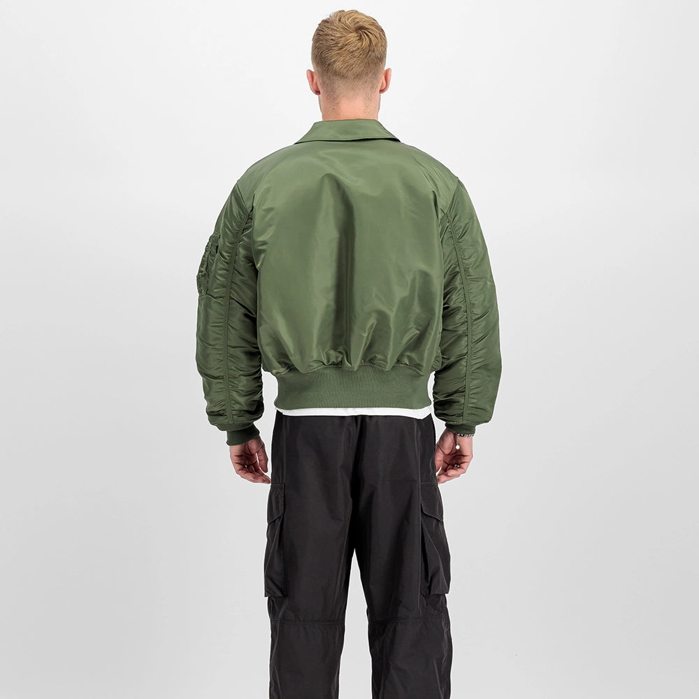 „Alpha Industries CWU 45 Heritage Bomberjacke in Sage Green mit Umlegekragen, Klettverschluss-Taschen und rotem Remove Before Flight Tag bei Stickabush Berlin.“