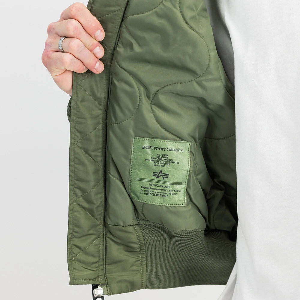 „Alpha Industries CWU 45 Heritage Bomberjacke in Sage Green mit Umlegekragen, Klettverschluss-Taschen und rotem Remove Before Flight Tag bei Stickabush Berlin.“