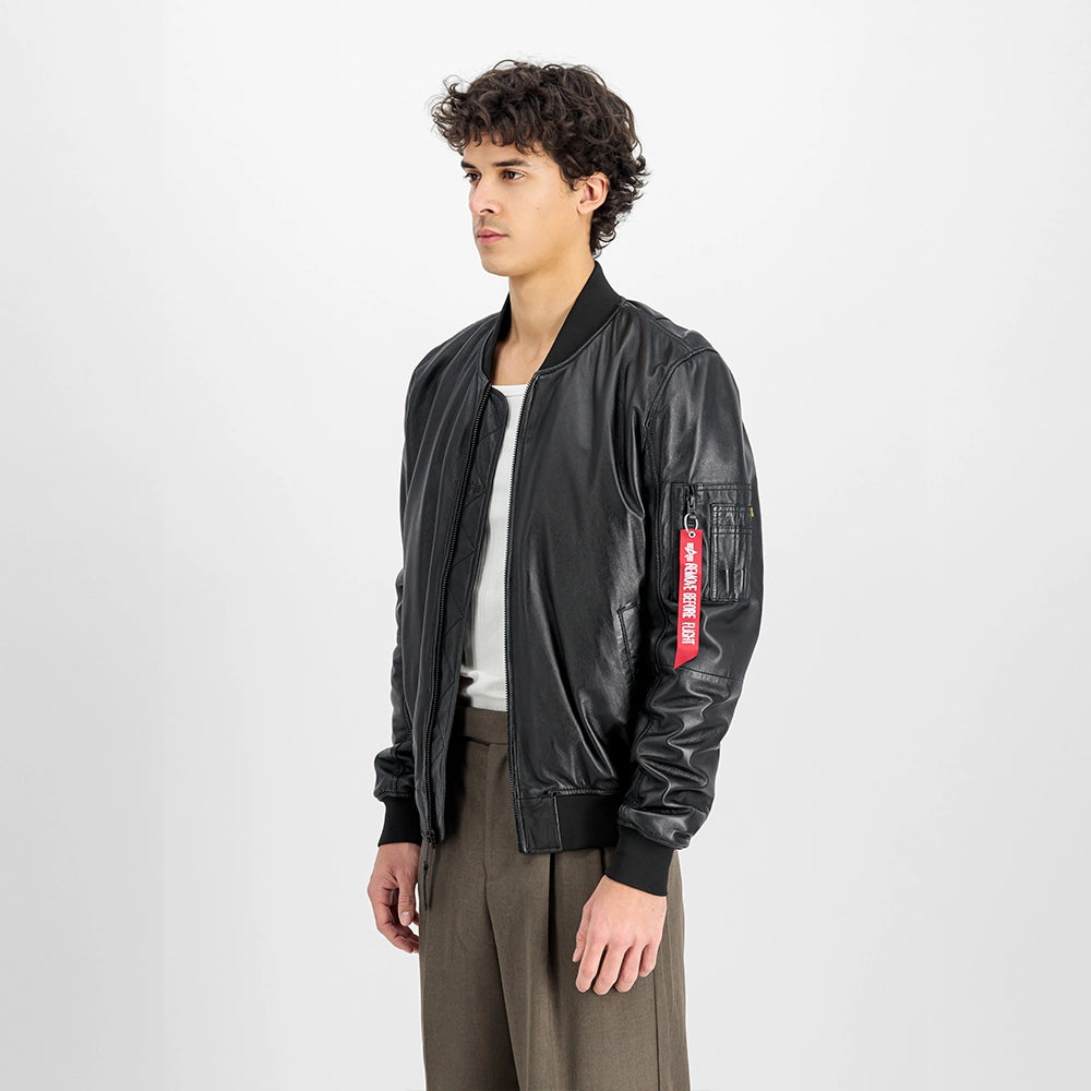 „Schwarze Alpha Industries MA-1 Lederjacke mit Strickkragen, Utility Pocket am Ärmel und rotem Remove Before Flight Tag vor neutralem Hintergrund bei Stickabush Berlin.“