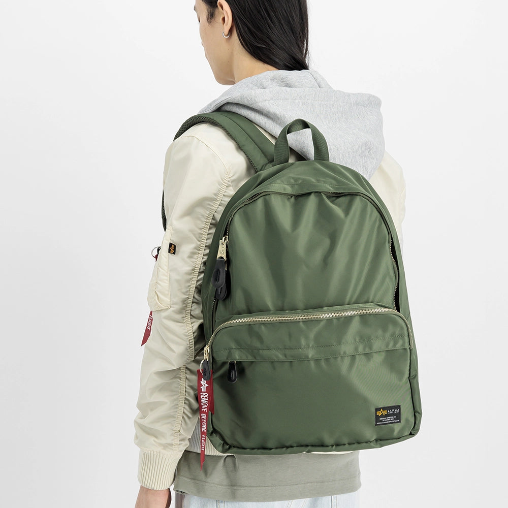 “Grüner (Sage Green) Alpha Industries Crew Backpack aus glänzendem Flight-Nylon mit rotem Remove Before Flight Tag und Utility-Tasche bei Stickabush Berlin.“