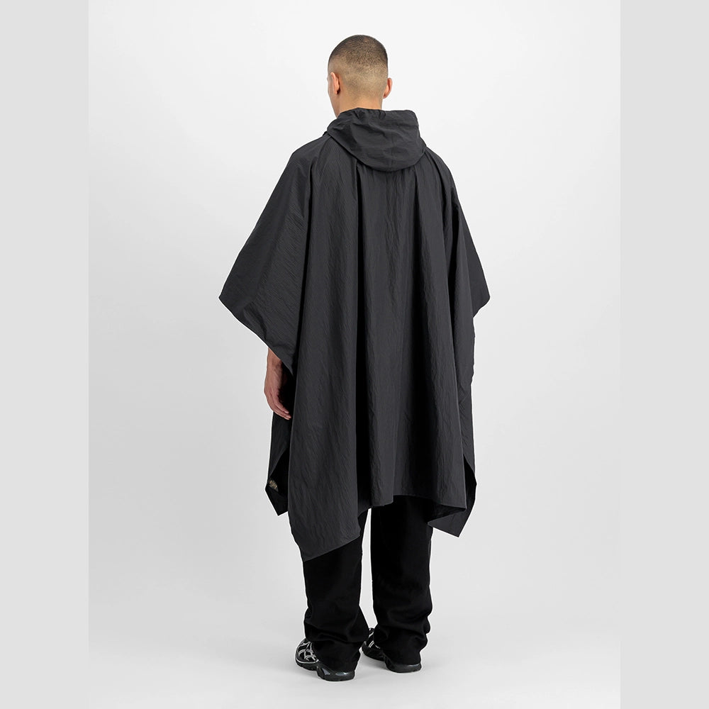 “Schwarzes Alpha Industries Packable Rain Cape mit Logo auf der Brust, verstellbarer Kapuze und rotem Remove Before Flight Anhänger bei Stickabush Berlin.“