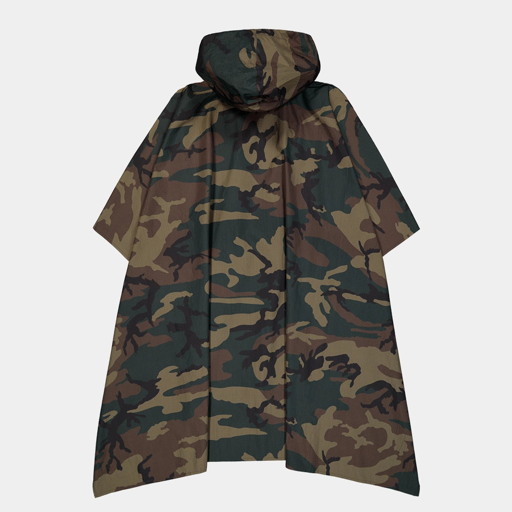 “Alpha Industries Regenponcho im Woodland Camouflage Muster mit verstellbarer Kapuze und rotem Remove Before Flight Anhänger bei Stickabush Berlin.“
