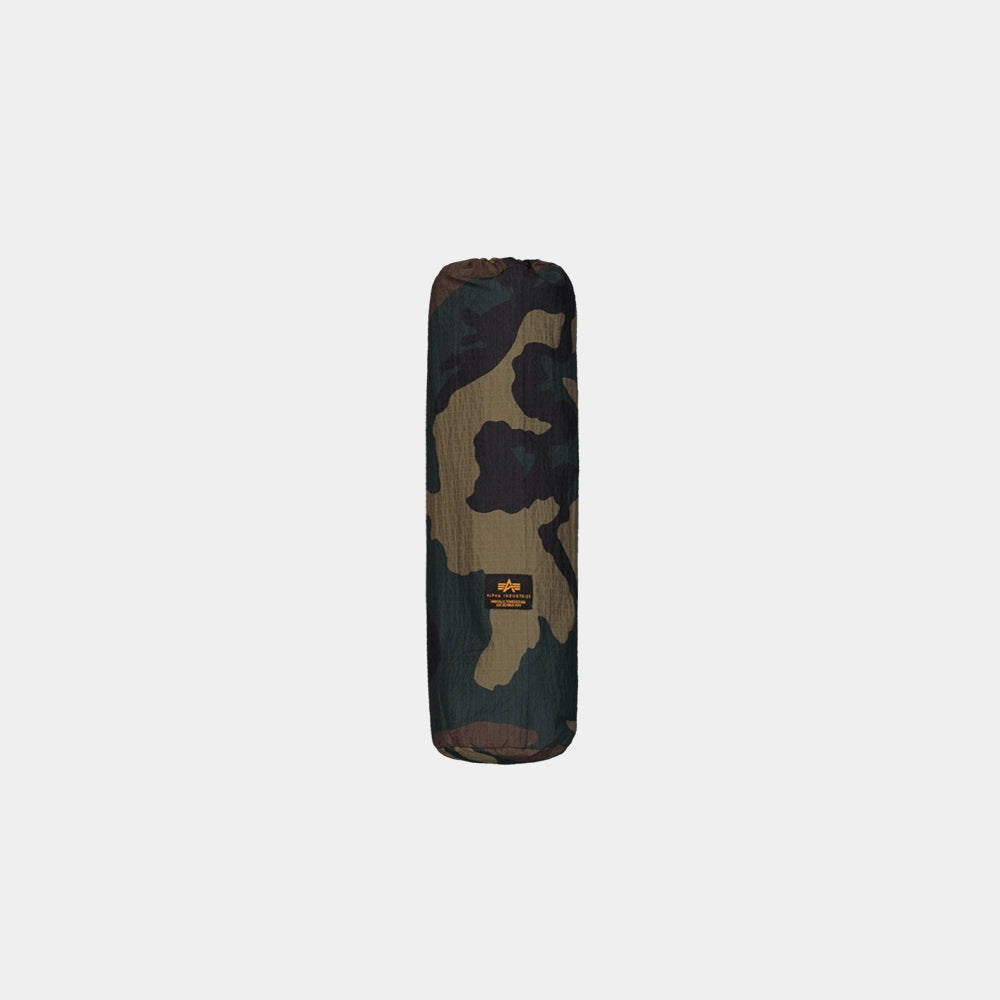 “Alpha Industries Regenponcho im Woodland Camouflage Muster mit verstellbarer Kapuze und rotem Remove Before Flight Anhänger bei Stickabush Berlin.“