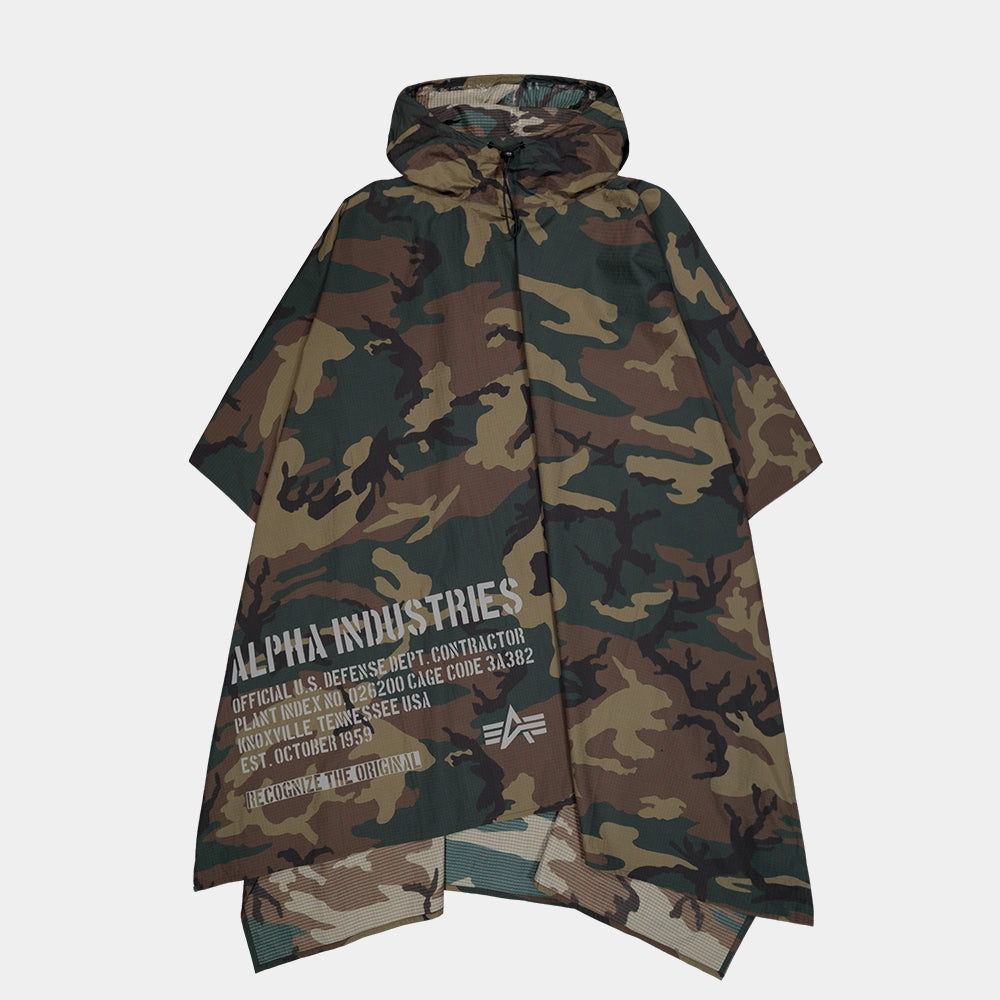 “Alpha Industries Regenponcho im Woodland Camouflage Muster mit verstellbarer Kapuze und rotem Remove Before Flight Anhänger bei Stickabush Berlin.“