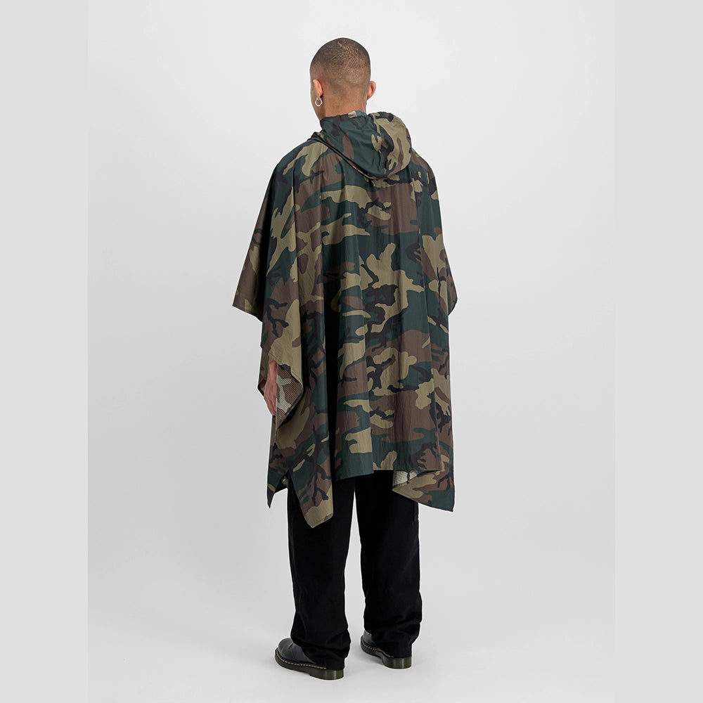 “Alpha Industries Regenponcho im Woodland Camouflage Muster mit verstellbarer Kapuze und rotem Remove Before Flight Anhänger bei Stickabush Berlin.“