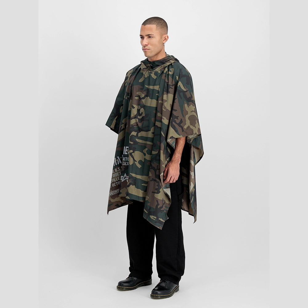 “Alpha Industries Regenponcho im Woodland Camouflage Muster mit verstellbarer Kapuze und rotem Remove Before Flight Anhänger bei Stickabush Berlin.“