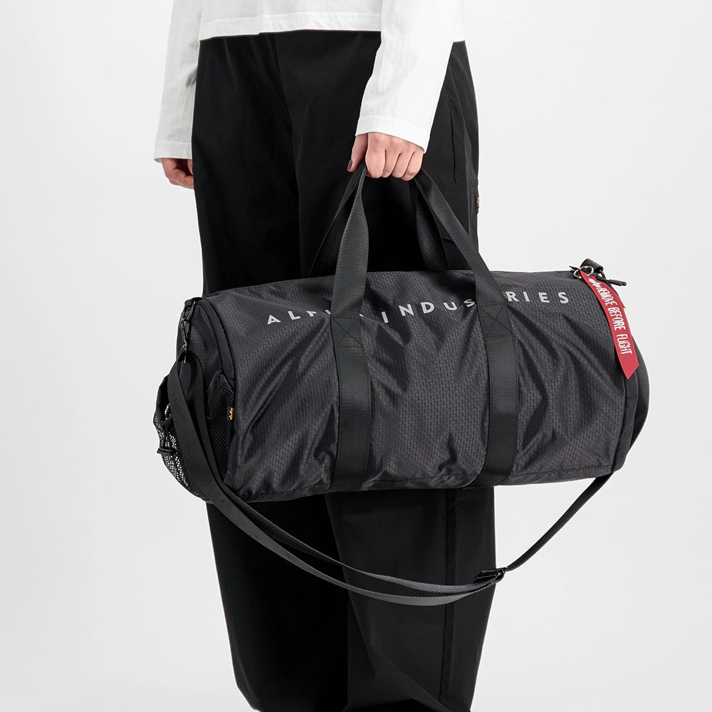 “Schwarze Alpha Industries Sporttasche aus Ripstop-Gewebe mit rotem Remove Before Flight Anhänger und stabilen Kordelzügen bei Stickabush Berlin.“