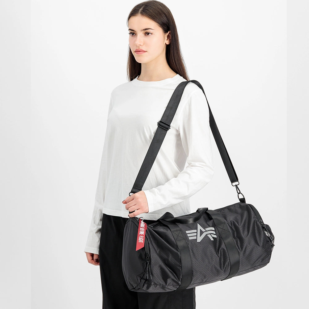 “Schwarze Alpha Industries Sporttasche aus Ripstop-Gewebe mit rotem Remove Before Flight Anhänger und stabilen Kordelzügen bei Stickabush Berlin.“