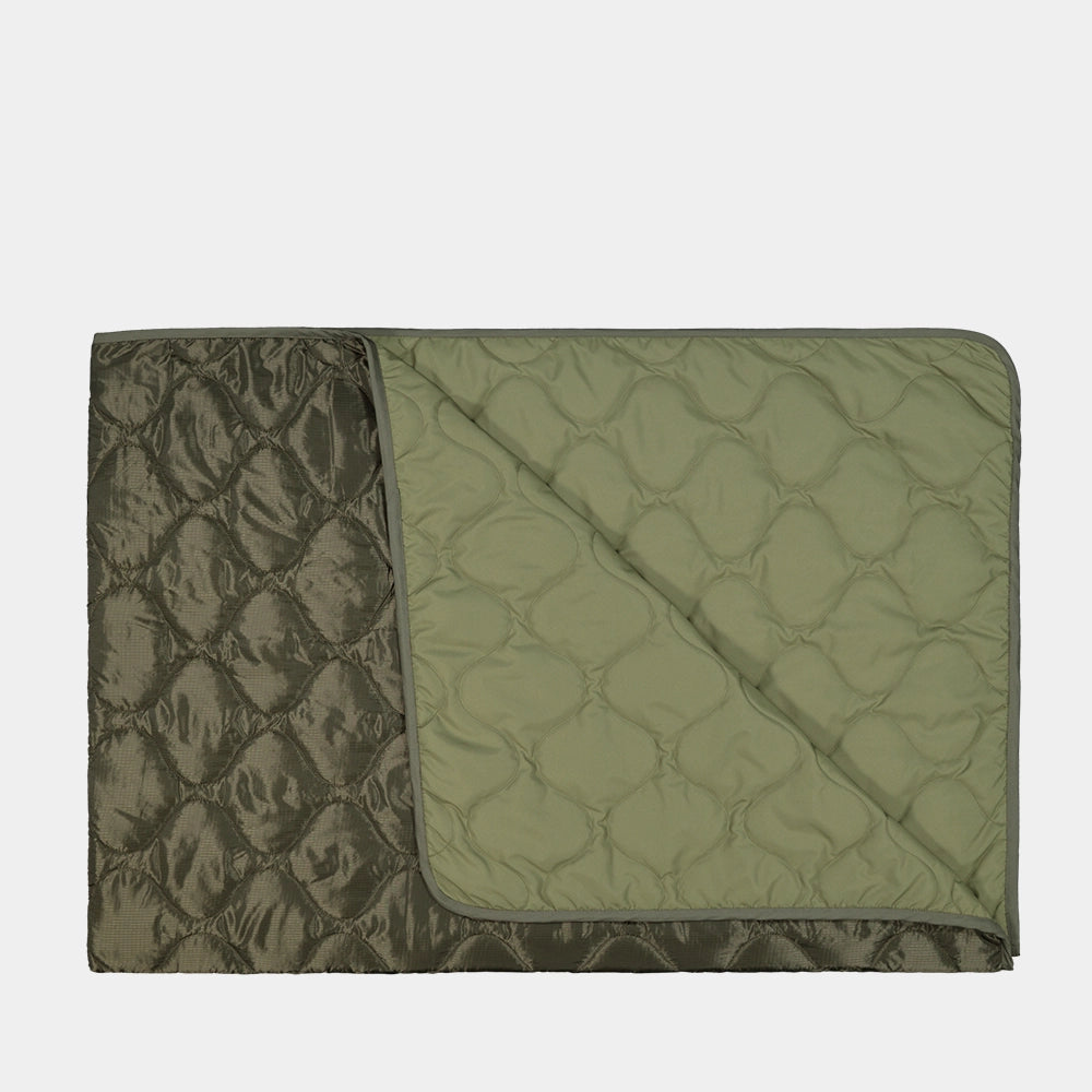 “Dunkelgrüne (Dark Olive) Alpha Industries Picknickdecke aus Flight-Nylon, zusammengefaltet in der integrierten Tasche mit rotem Remove Before Flight Tag bei Stickabush Berlin.“