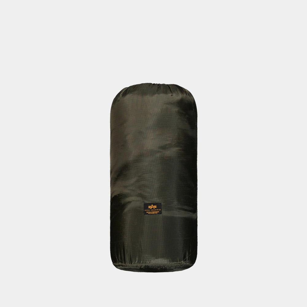 “Dunkelgrüne (Dark Olive) Alpha Industries Picknickdecke aus Flight-Nylon, zusammengefaltet in der integrierten Tasche mit rotem Remove Before Flight Tag bei Stickabush Berlin.“