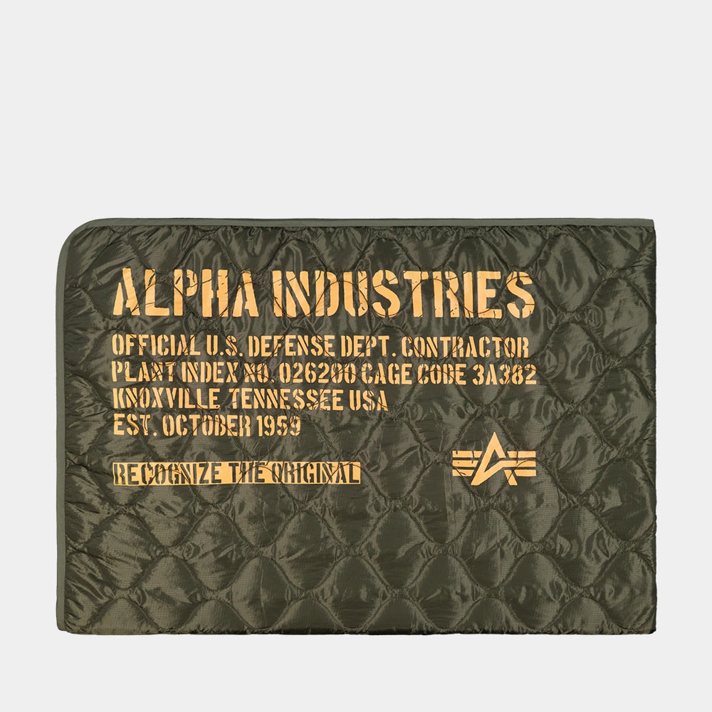 “Dunkelgrüne (Dark Olive) Alpha Industries Picknickdecke aus Flight-Nylon, zusammengefaltet in der integrierten Tasche mit rotem Remove Before Flight Tag bei Stickabush Berlin.“