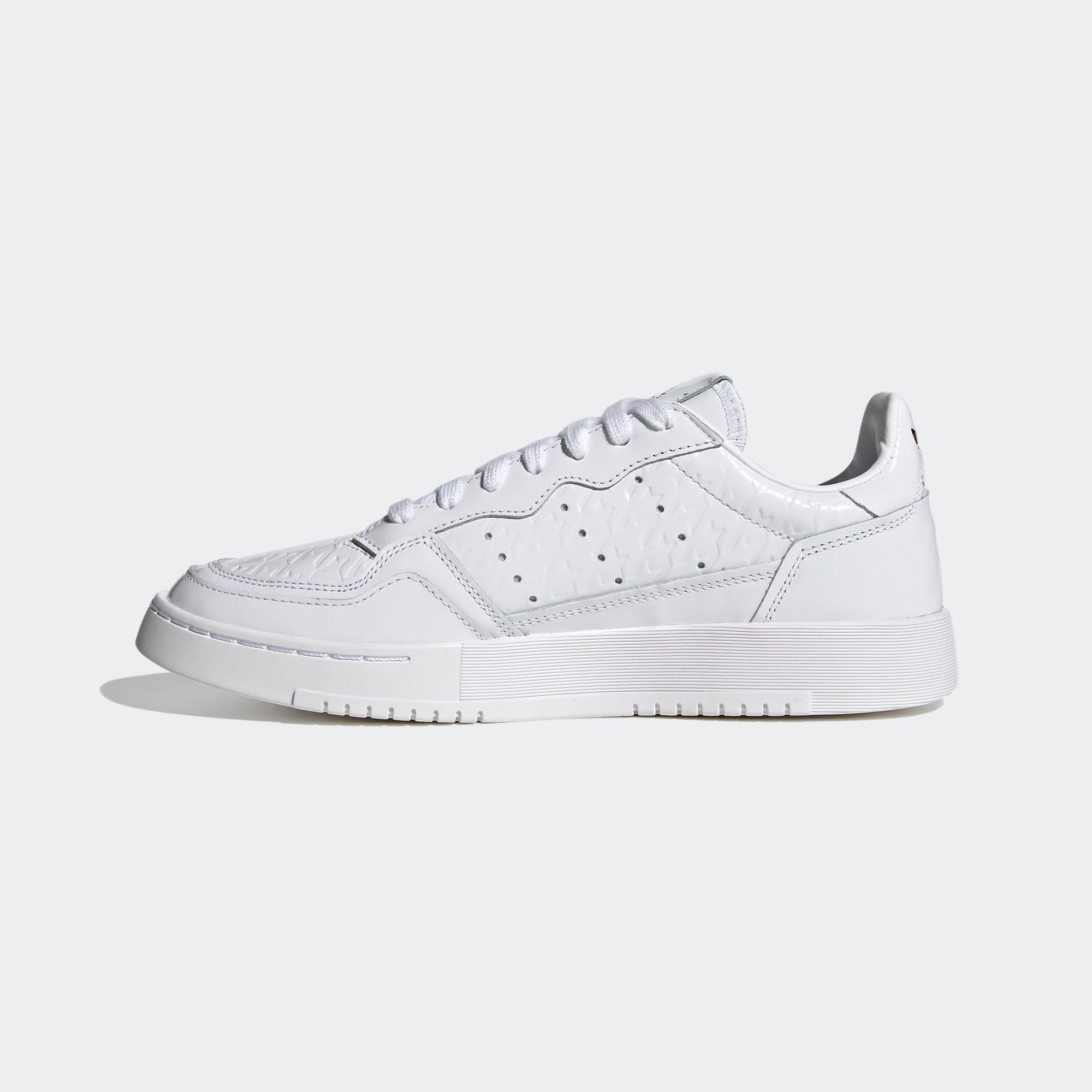Adidas Supercourt W. Weißer Sneaker aus Leder, mit goldenen Metall-Akzenten, Ziernähten, perforierten 3-Stripes und einer Gummisohle.