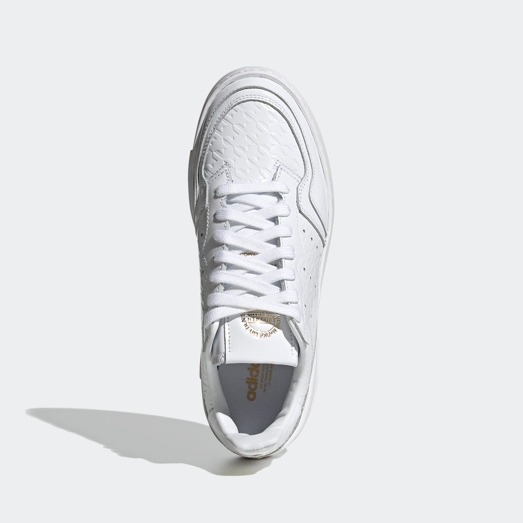 Adidas Supercourt W. Weißer Sneaker aus Leder, mit goldenen Metall-Akzenten, Ziernähten, perforierten 3-Stripes und einer Gummisohle.