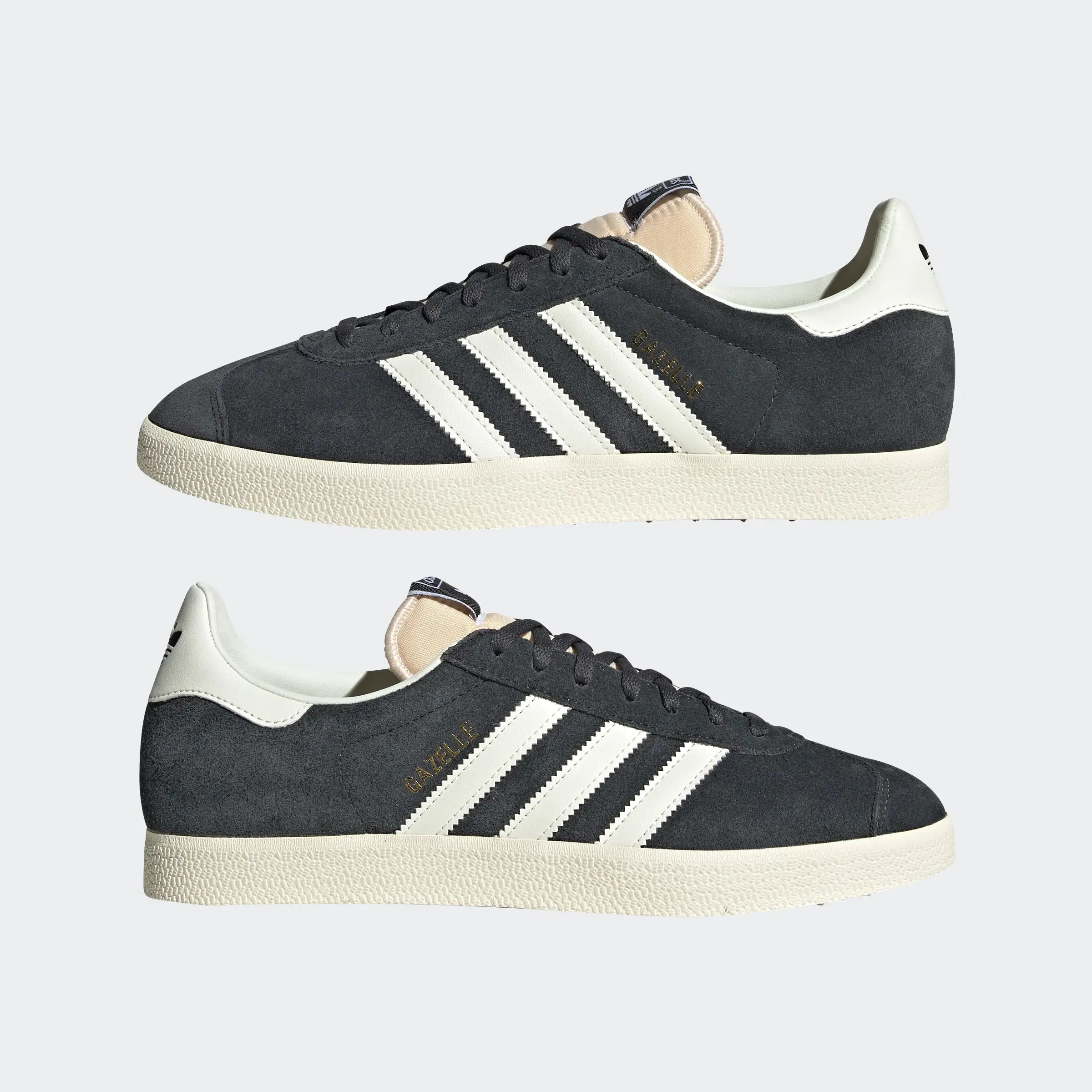 "Anthrazitfarbene Adidas Gazelle Schuhe mit off-weißen Streifen und cremefarbener Sohle. Klassisches Wildleder-Obermaterial, goldener 'Gazelle' Schriftzug an der Seite."