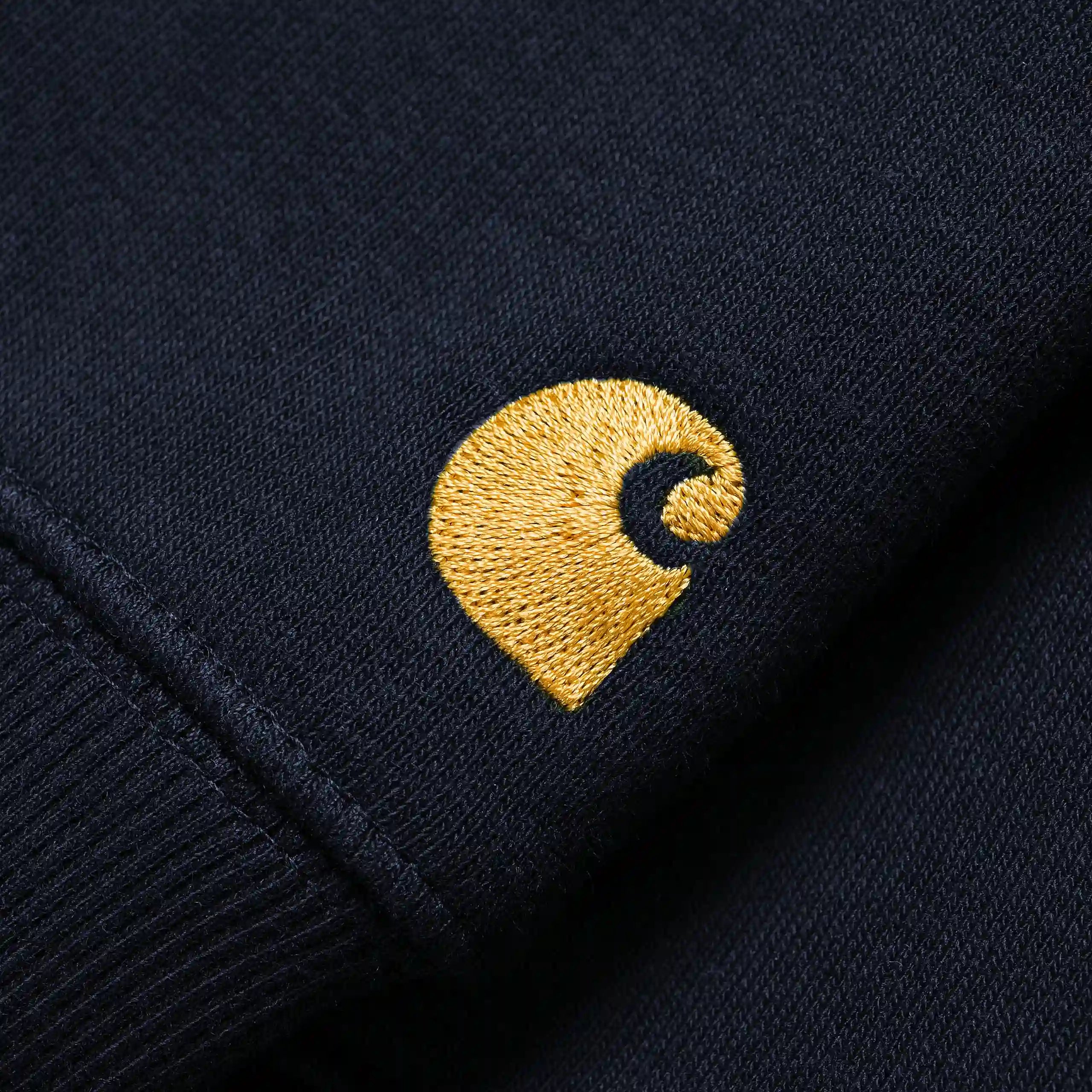 „Dunkelblaues Carhartt WIP Chase Sweatshirt mit goldenem Carhartt C-Logo-Stitch am Ärmel und Rundhalsausschnitt bei Stickabush Berlin."