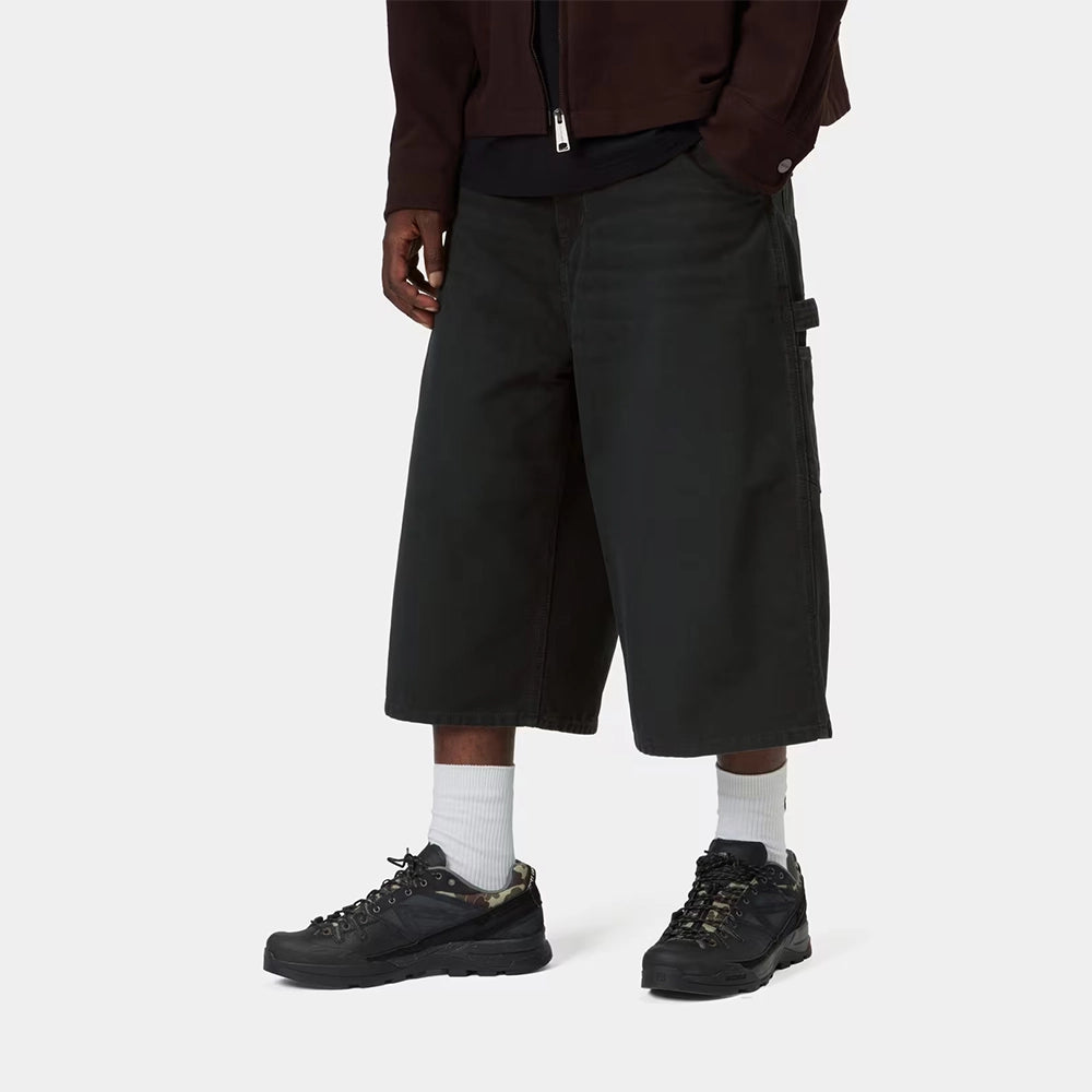 Carhartt WIP OG Single Knee Long Short in Black – Vorderansicht am Model der schwarzen Canvas-Workwear-Shorts mit Tool-Taschen und Hammerlasche.