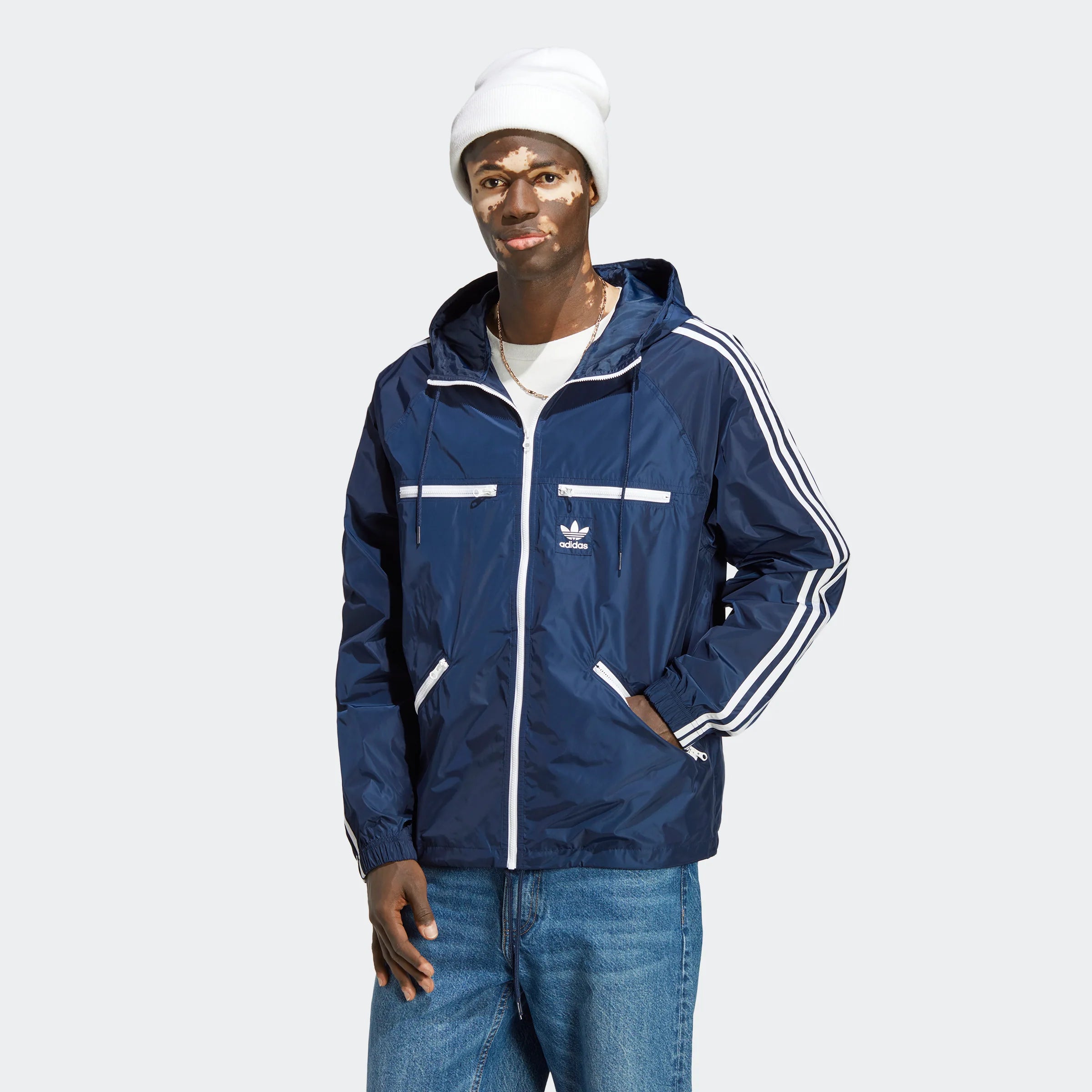 Adidas Classics Windbreaker – Night Indigo / White. Dunkelblauer Windbreaker aus recyceltem Polyester, mit weißem 3-Streifen-Design, Stehkragen und Kängurutasche.