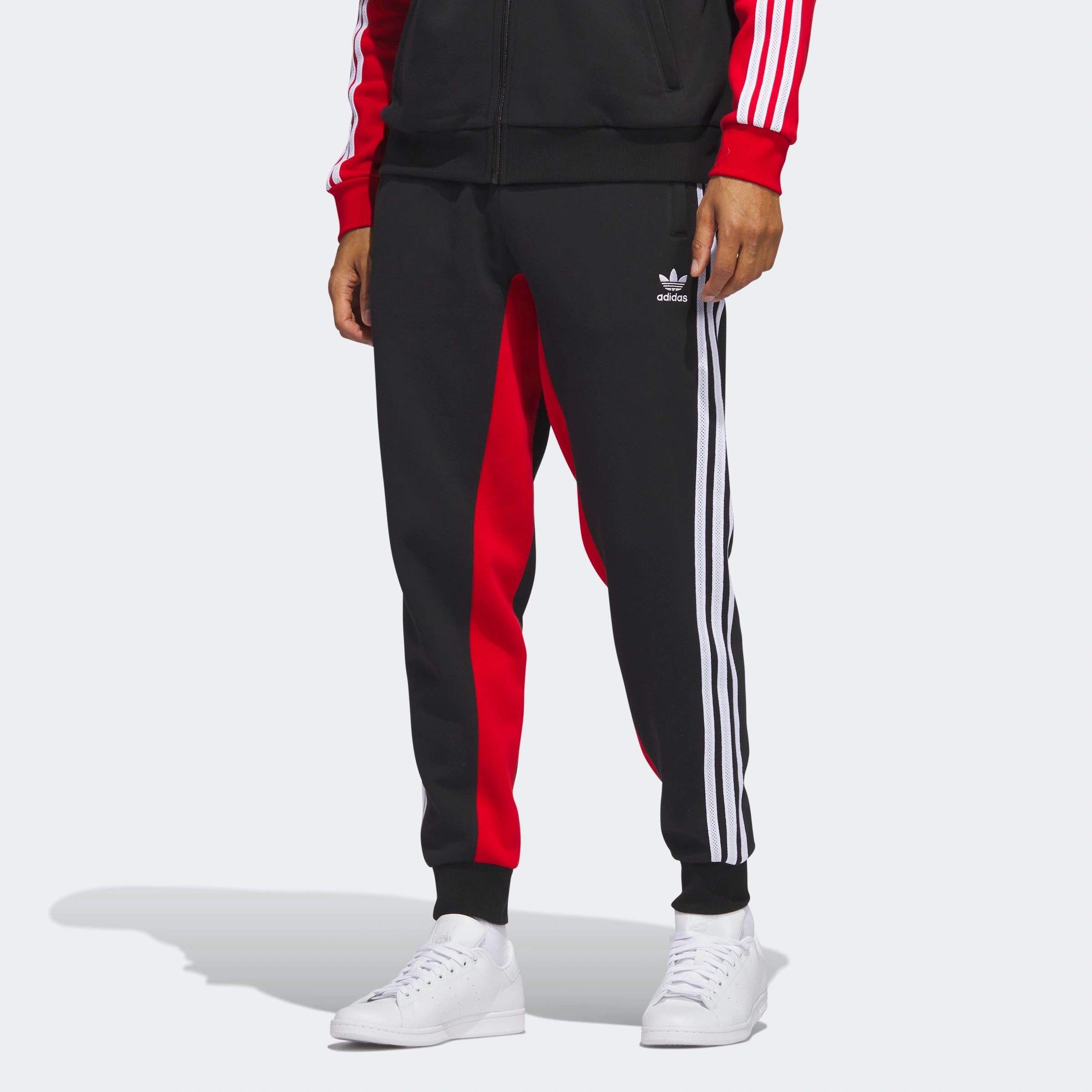 "Schwarze Adidas Fleece-Trainingshose mit roten seitlichen Streifen. Weiches Fleece-Material, elastischer Bund mit Kordelzug, offene Beinabschlüsse."