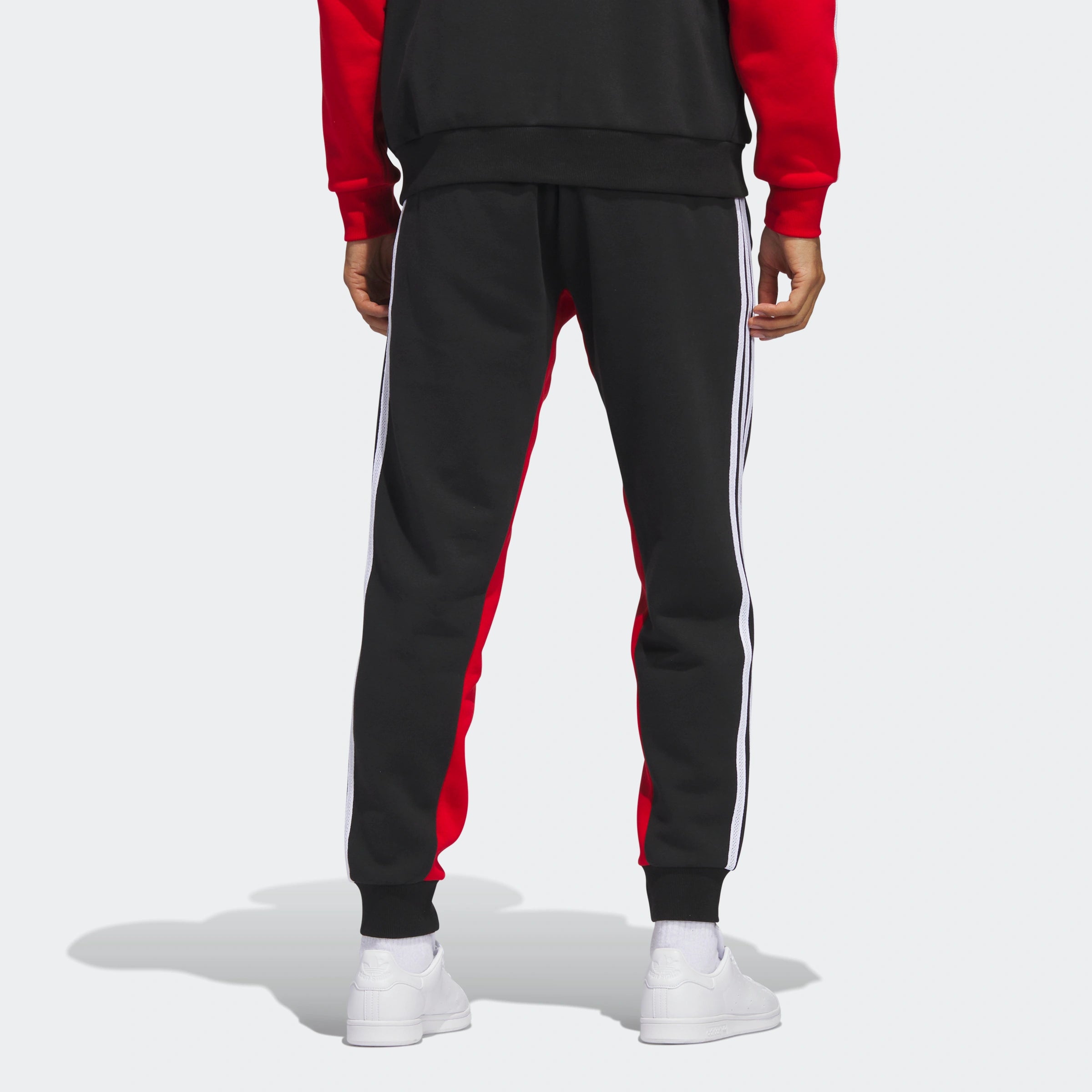 "Schwarze Adidas Fleece-Trainingshose mit roten seitlichen Streifen. Weiches Fleece-Material, elastischer Bund mit Kordelzug, offene Beinabschlüsse."