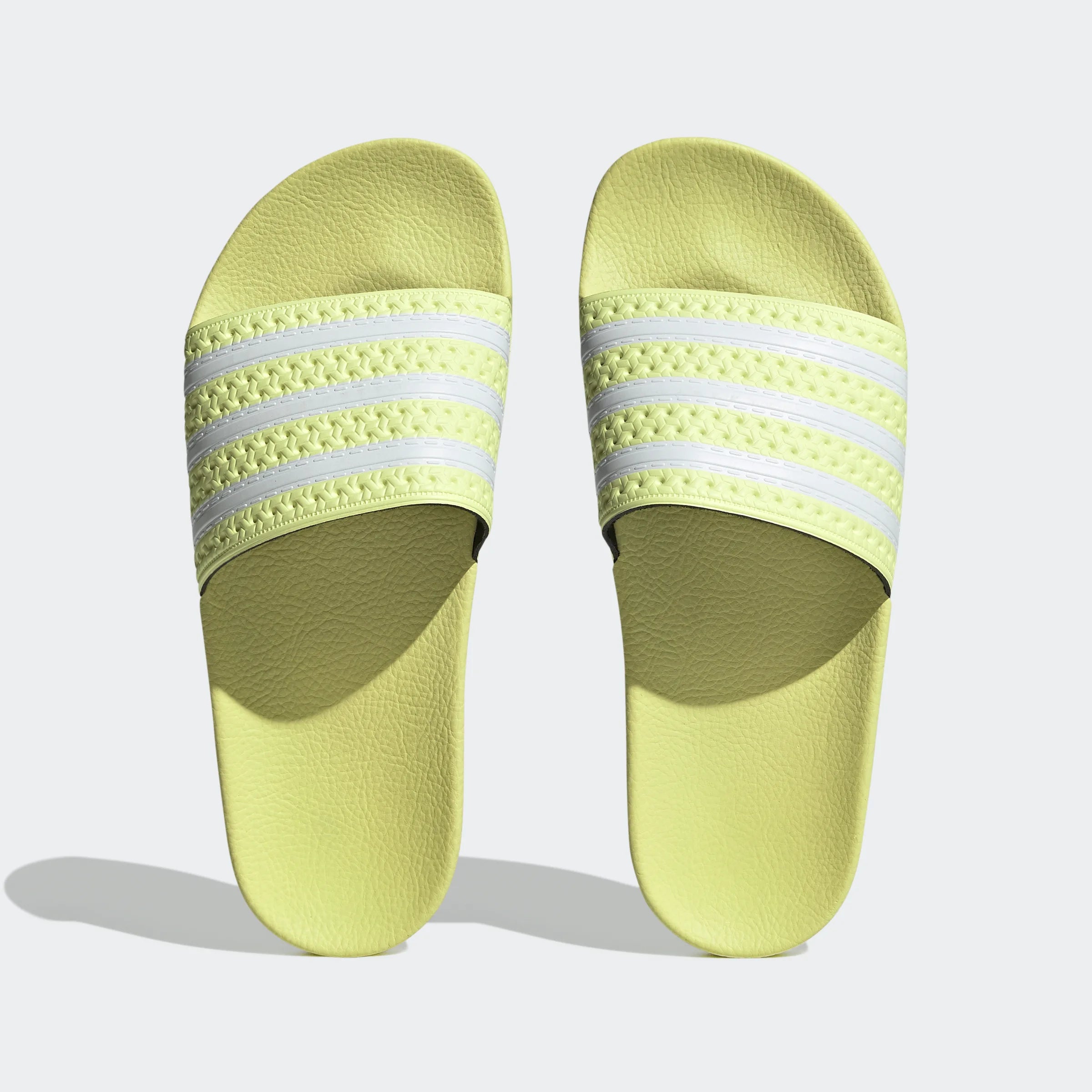 "Gelbe Adidas Adilette für Damen mit weißen Details. Klassische Badesandale mit breitem Riemen und weißem Adidas Logo. Bequemes, leichtes Material."