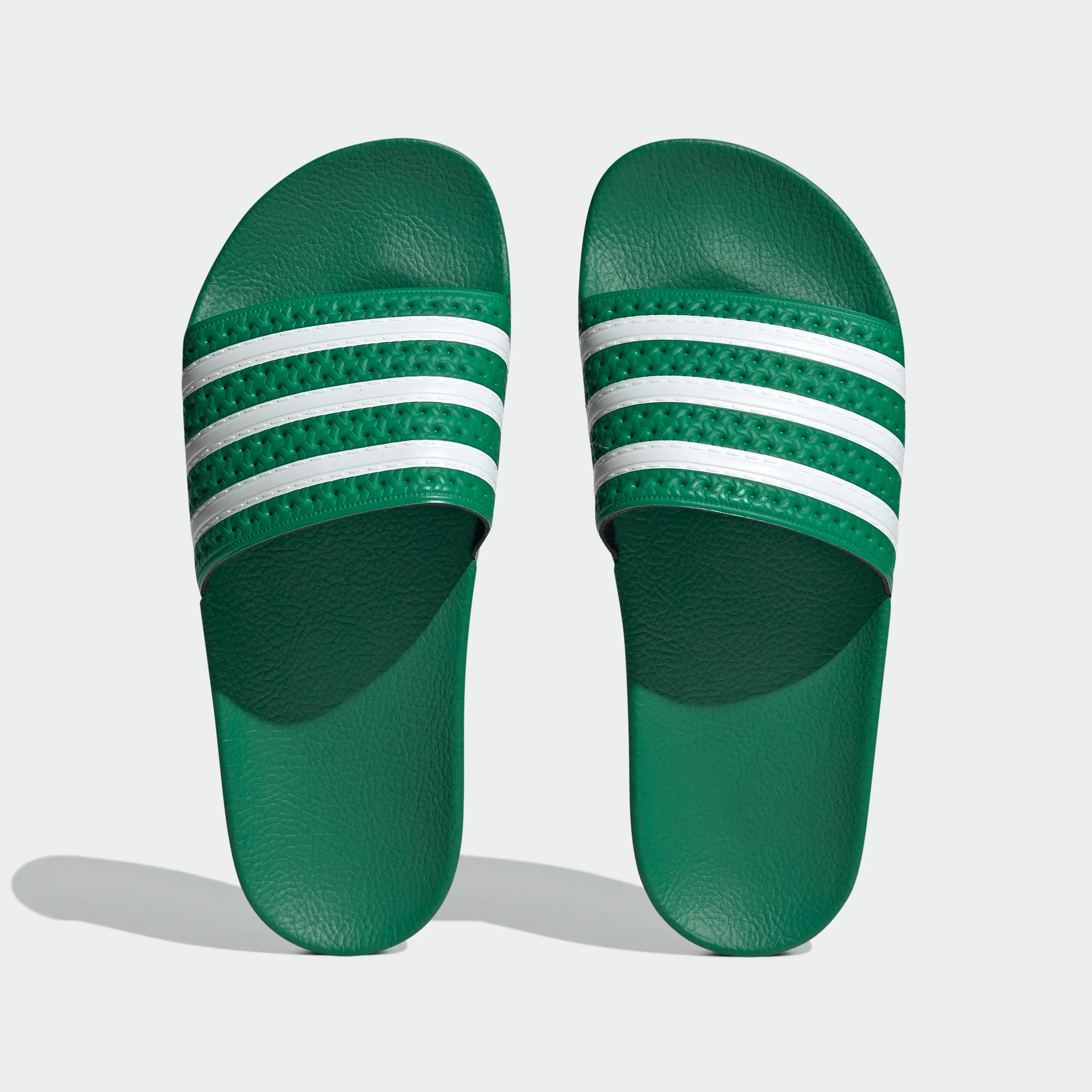 "Grüne Adidas Adilette für Damen mit weißen Details. Klassische Badesandale mit breitem Riemen und weißem Adidas Logo. Bequemes, leichtes Material."