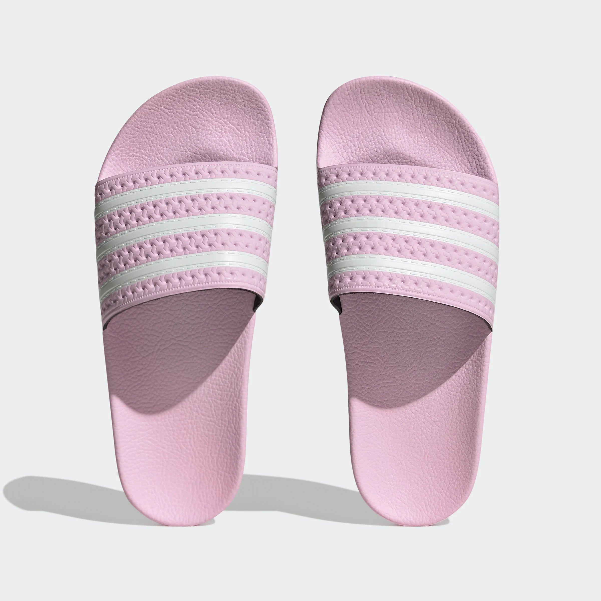"Rosafarbene Adidas Adilette für Damen mit weißen Details. Klassische Badesandale mit breitem Riemen und weißem Adidas Logo. Bequemes, leichtes Material."