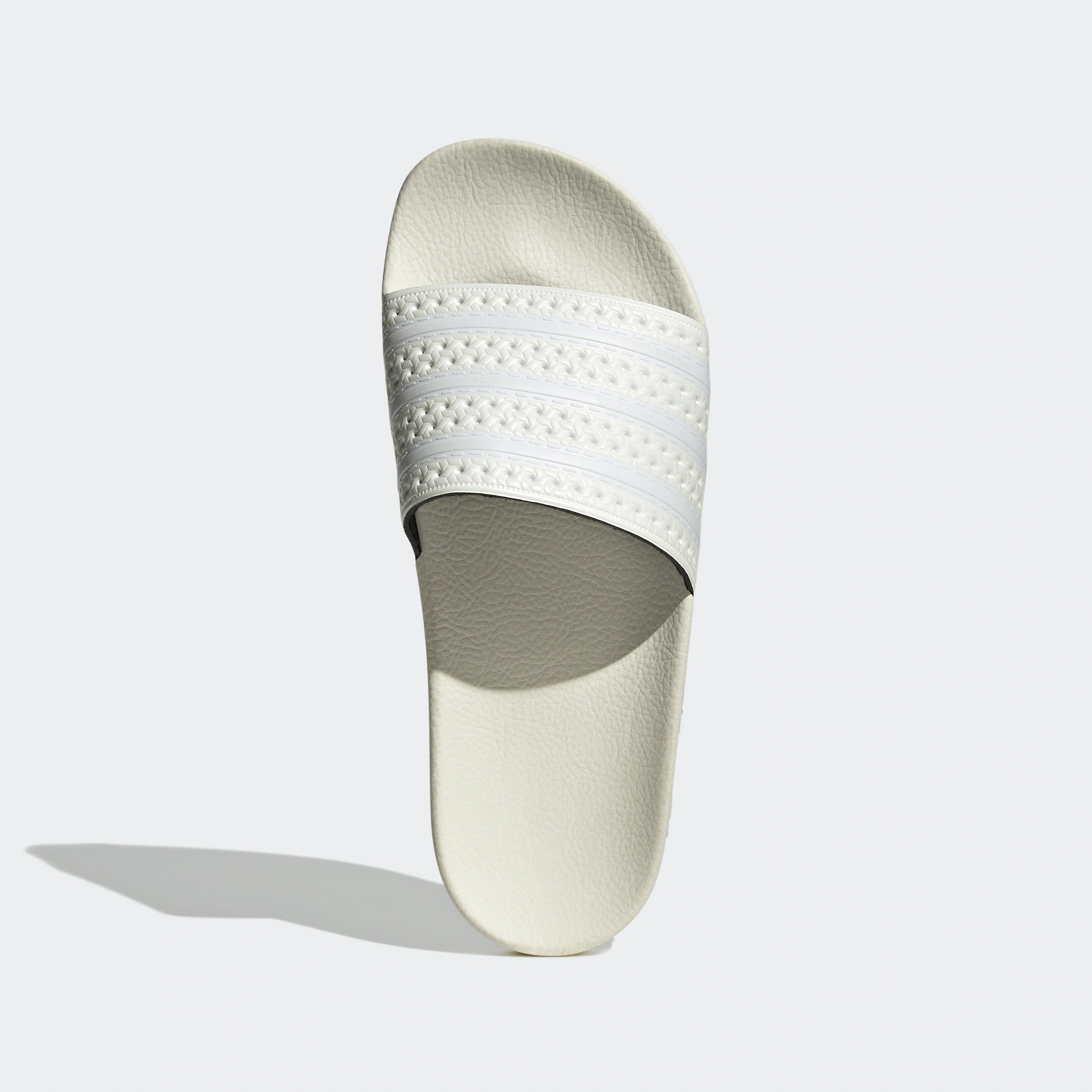"Off-weiße Adidas Adilette für Damen. Klassische Badesandale mit breitem Riemen und Adidas Logo in derselben Farbe. Bequemes, leichtes Material."