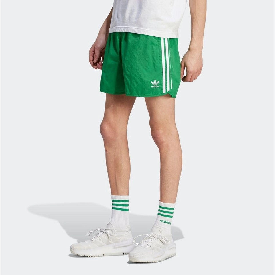 "Adidas Classics Sprinter Shorts. Kurze, grüne Shorts aus recyceltem Polyester, mit elastischem Bund, drei weißen Seitenstreifen und gesticktem Trefoil-Logo bei Stickabush Berlin."