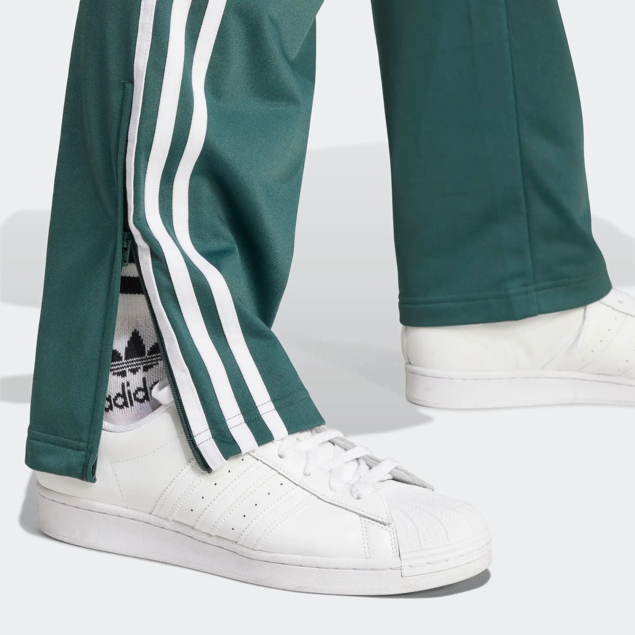 "Adidas Firebird Track Pants in Mineral Green/Weiß, Polyester, klassische Trainingshose mit weißen Streifen, grüne Farbe."