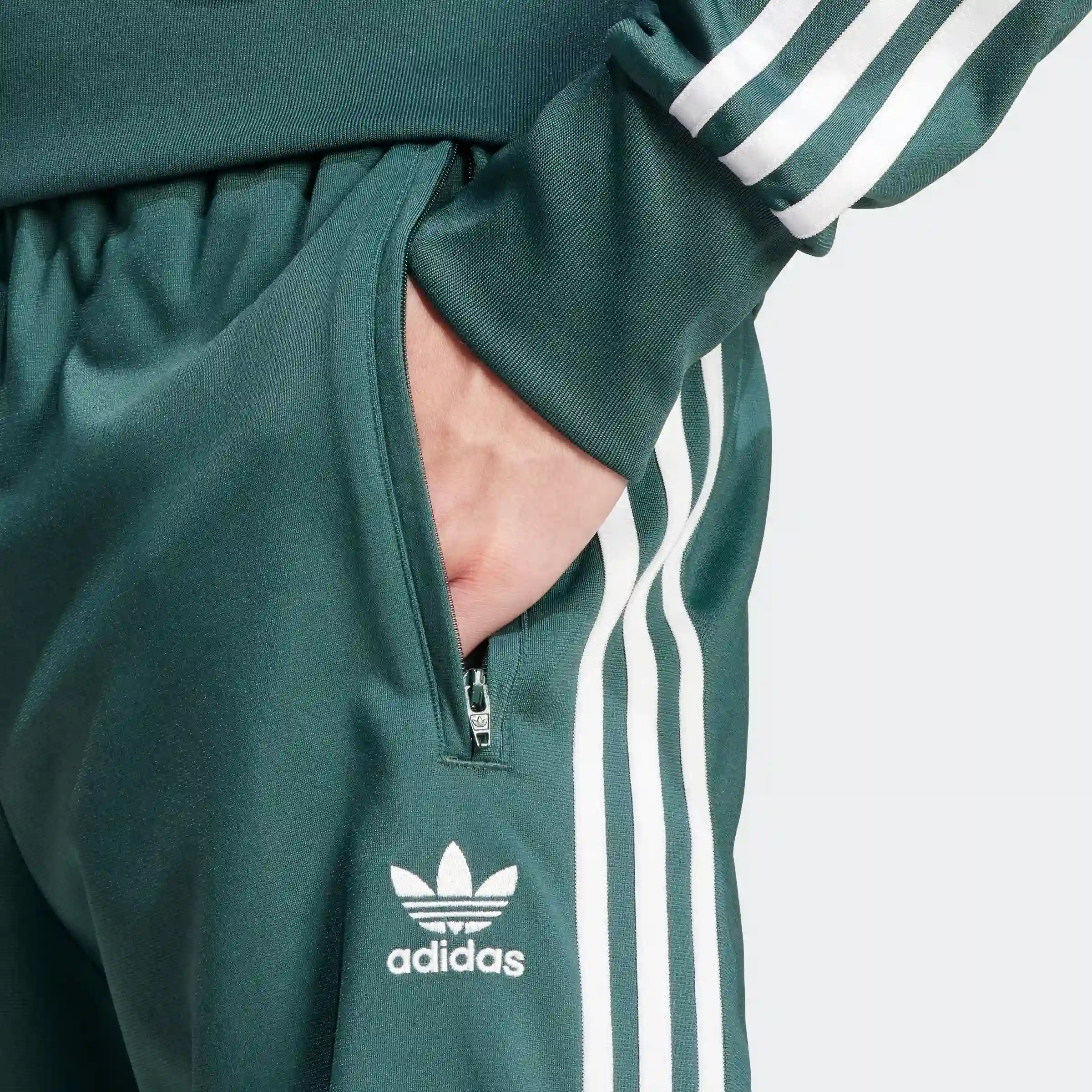 "Adidas Firebird Track Pants in Mineral Green/Weiß, Polyester, klassische Trainingshose mit weißen Streifen, grüne Farbe."