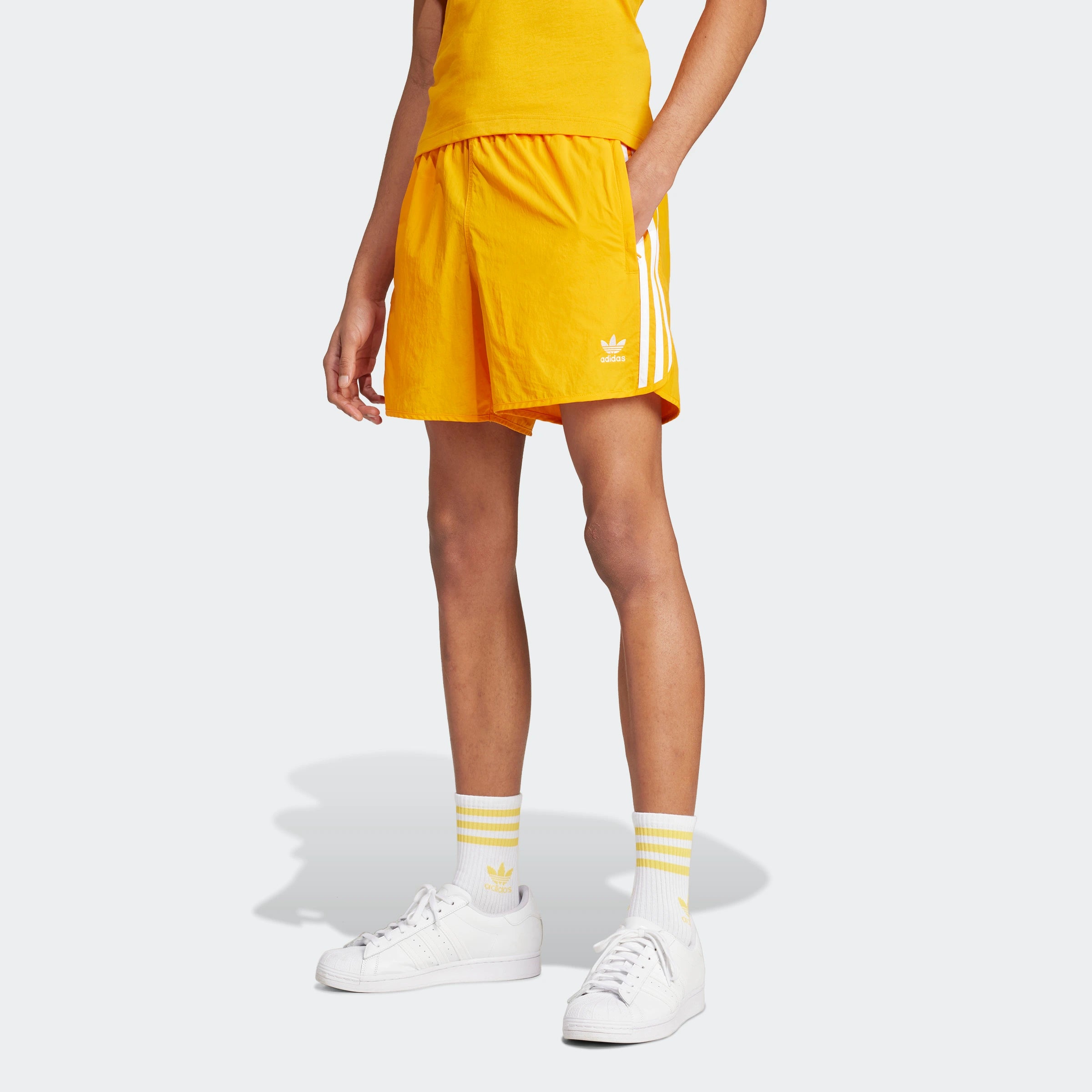 "Leuchtend orangefarbene Adidas Sprinter Shorts. Kurze, sportliche Hose mit elastischem Bund und kleinem, farblich passendem Adidas Logo am Bein."
