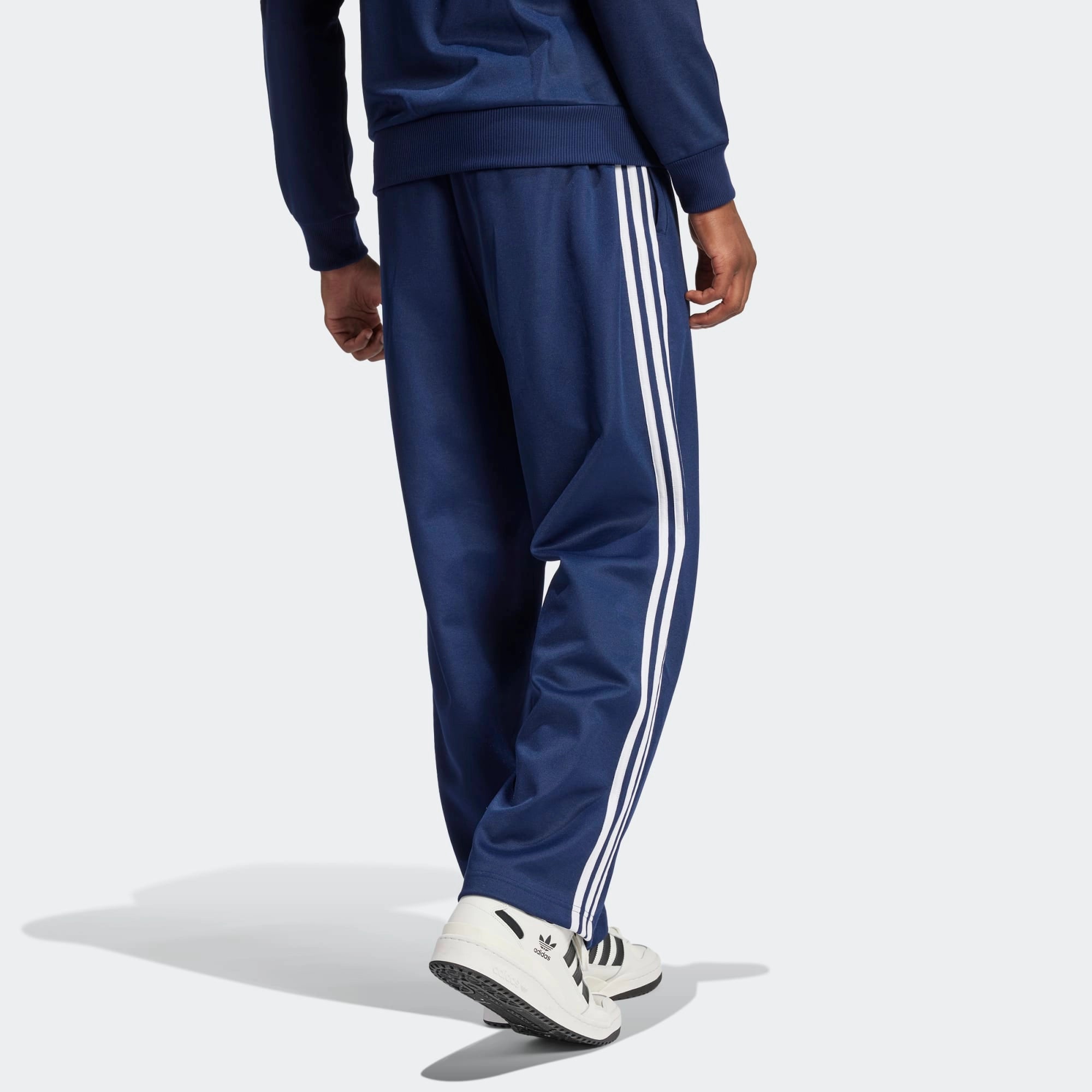 "Dunkelblaue Adidas Originals Baggy Fit Firebird Trainingshose mit weißen Streifen und weitem Beinverlauf bei Stickabush Berlin.“