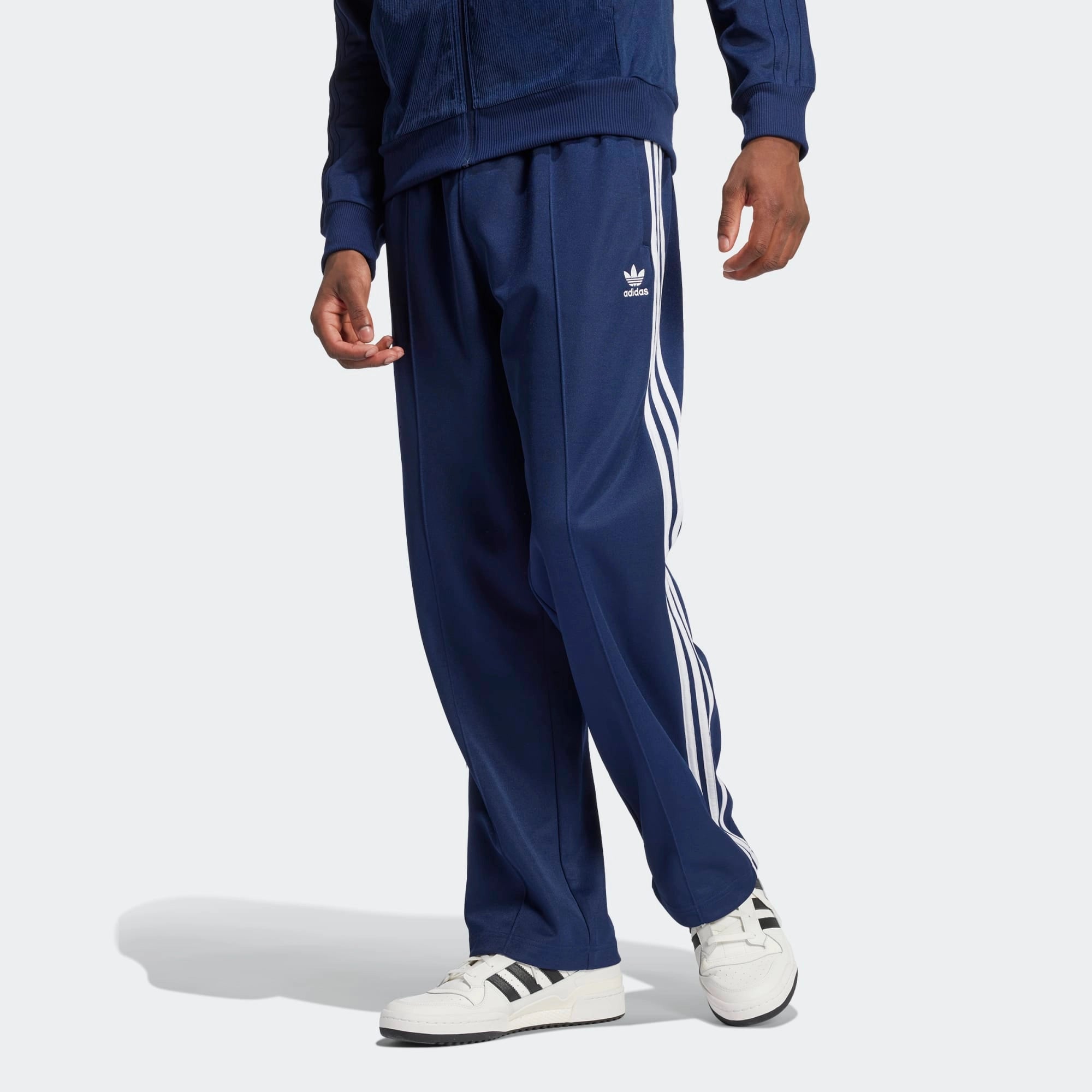 "Dunkelblaue Adidas Originals Baggy Fit Firebird Trainingshose mit weißen Streifen und weitem Beinverlauf bei Stickabush Berlin.“
