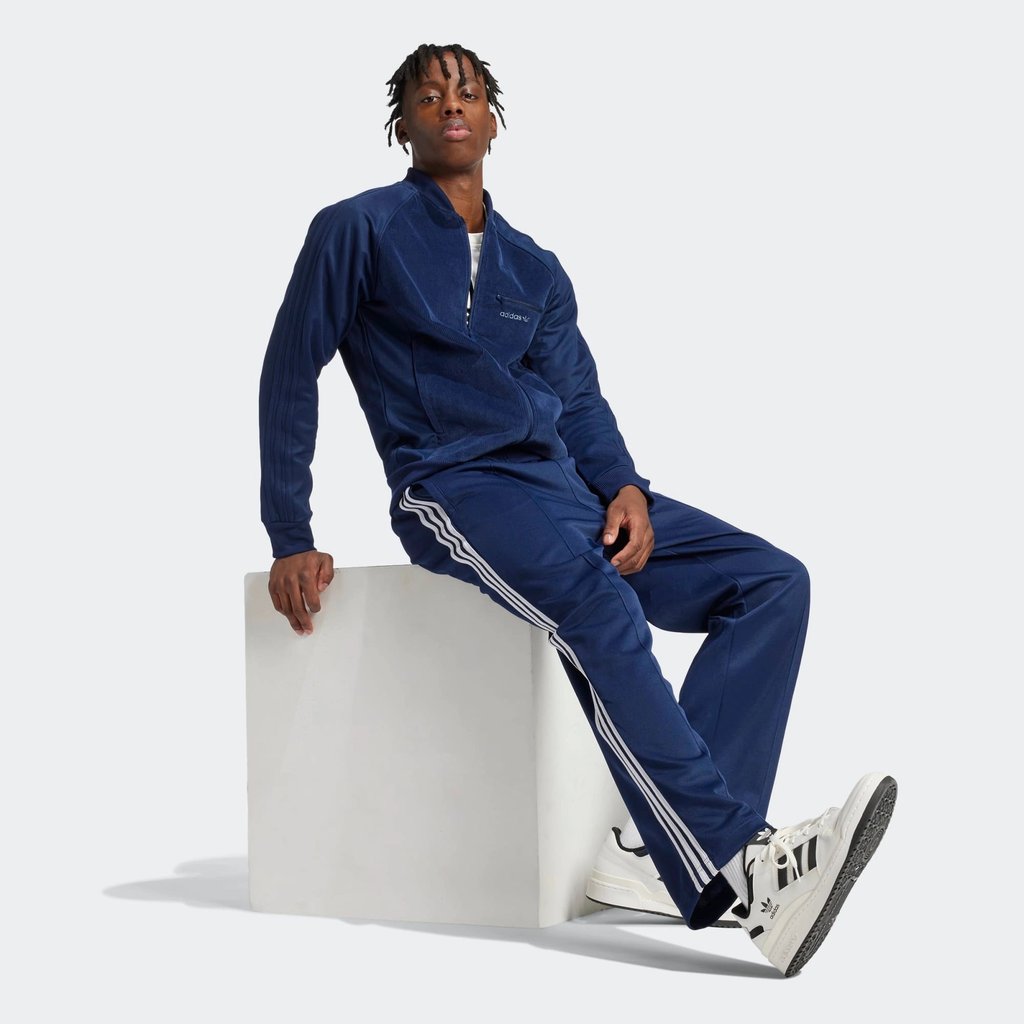 "Dunkelblaue Adidas Originals Baggy Fit Firebird Trainingshose mit weißen Streifen und weitem Beinverlauf bei Stickabush Berlin.“