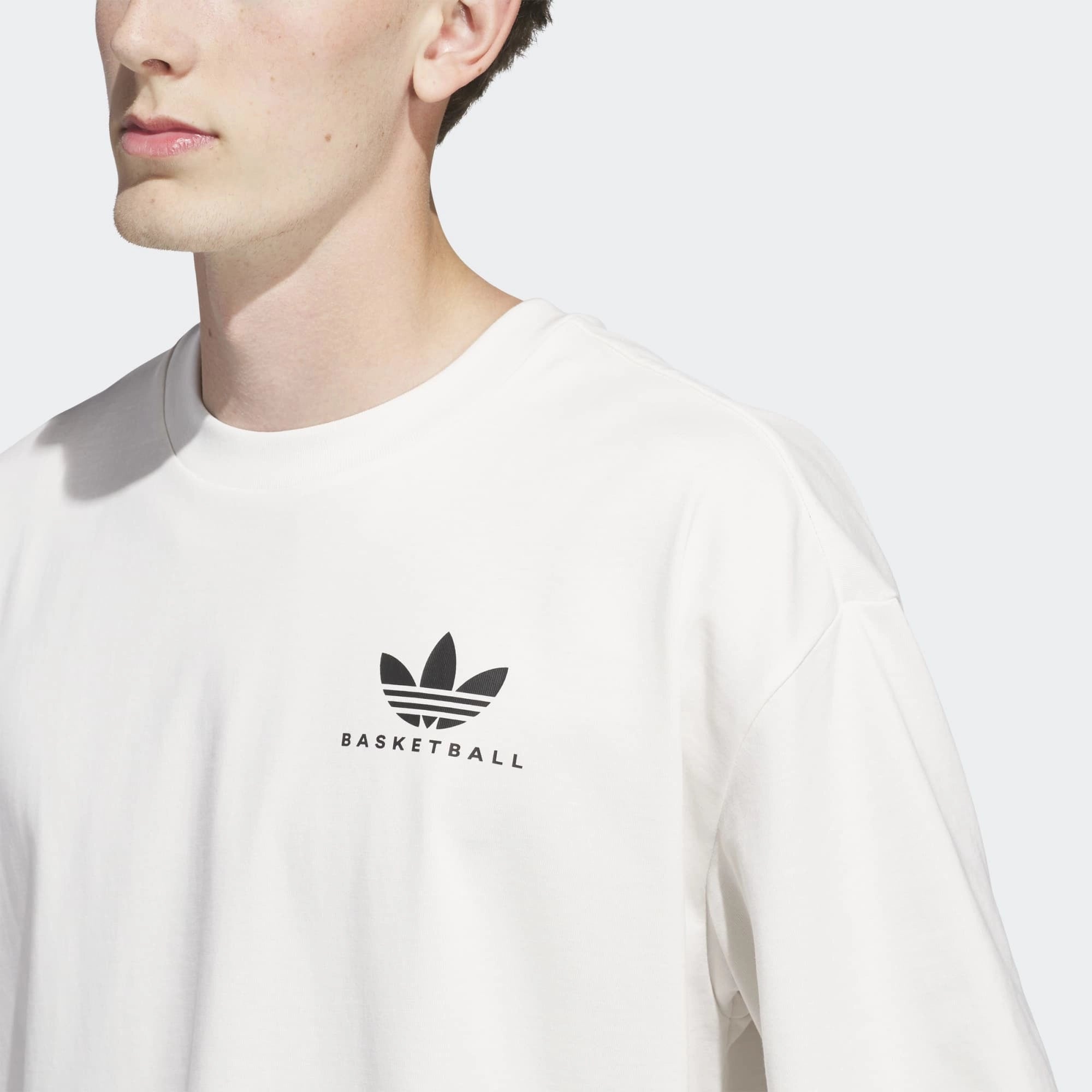„Frontansicht Print Model des Adidas Originals Worldwide Hoops GFX Tee in Cloud White – Weißes Baumwoll-T-Shirt mit schwarzem Basketball-Grafikprint bei Stickabush Berlin.“