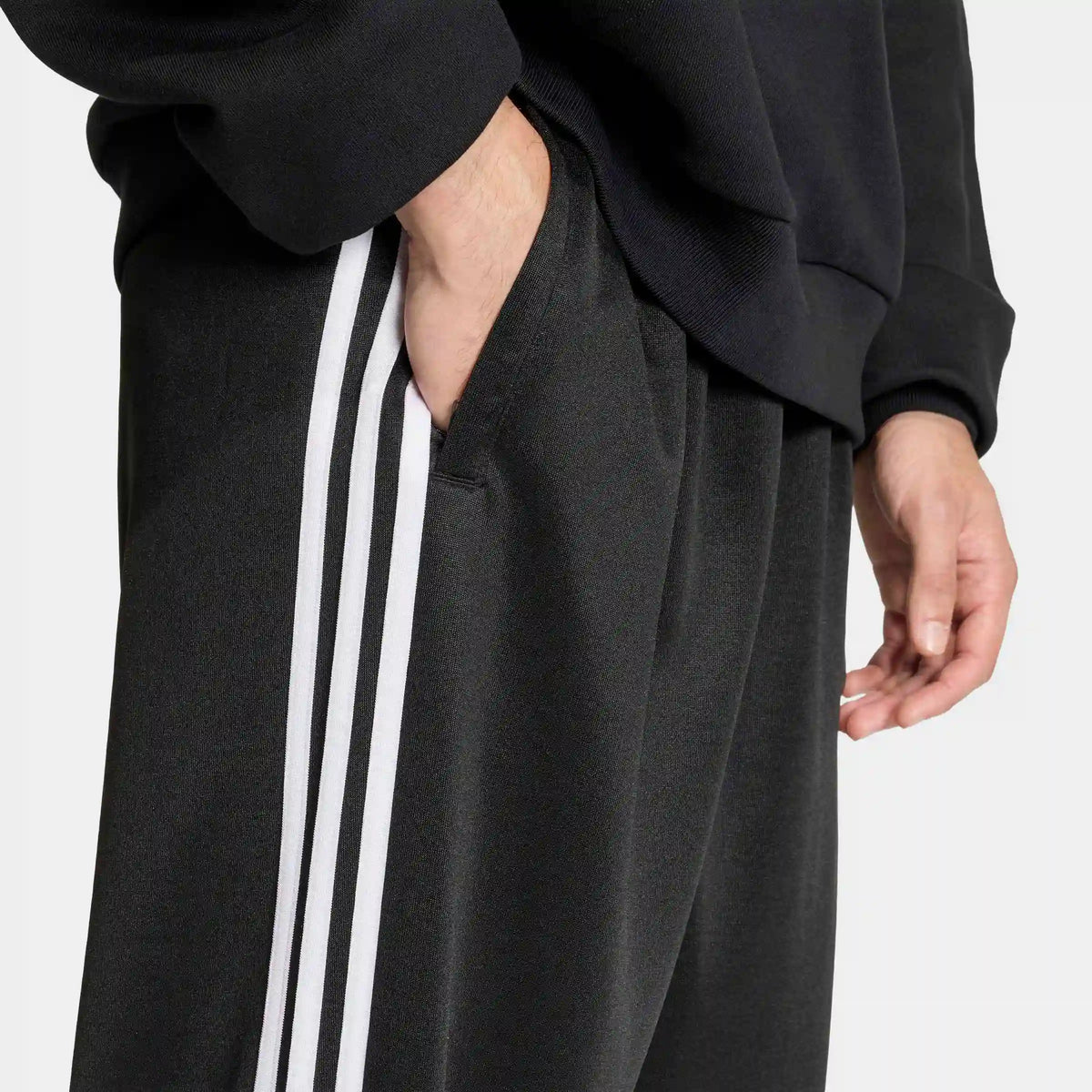 adidas Originals Adicolor Loose Tracksuit Pants in Black – Vorderansicht am Model der schwarzen Trainingshose mit den ikonischen 3-Stripes und lockerem Schnitt.