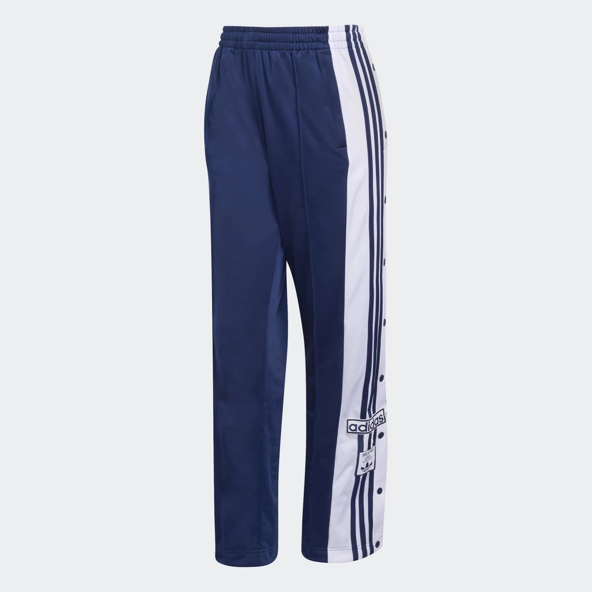 „Dunkelblaue Adidas Originals Adibreak Trainingshose für Damen (Night Indigo) mit durchgehenden Druckknöpfen und weißen Streifen bei Stickabush Berlin.“