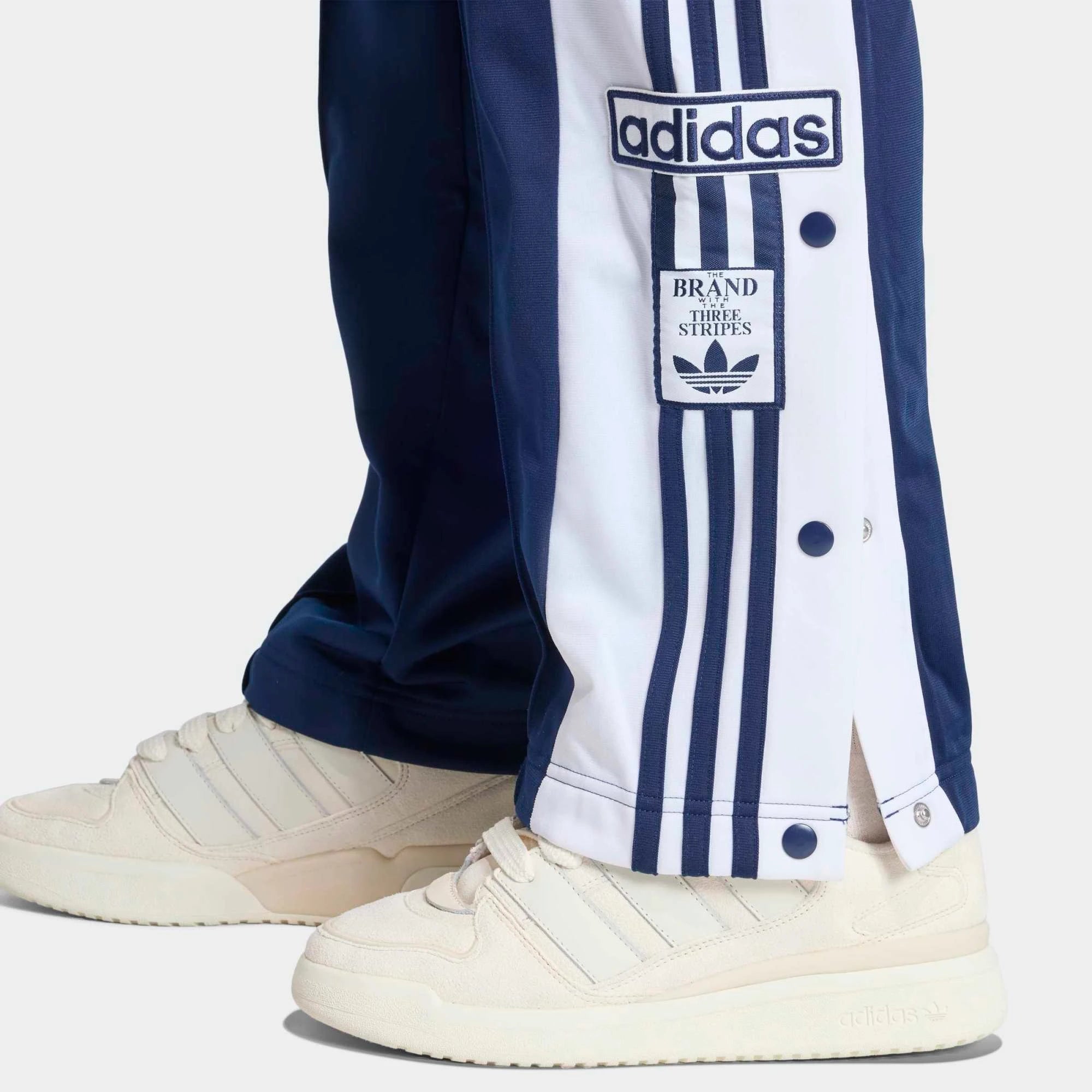 „Dunkelblaue Adidas Originals Adibreak Trainingshose für Damen (Night Indigo) mit durchgehenden Druckknöpfen und weißen Streifen bei Stickabush Berlin.“