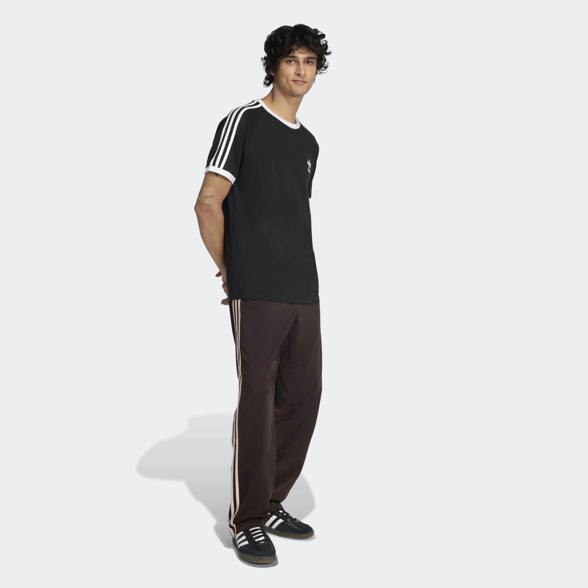 “Frontansicht Model Outfit der Adidas Originals Firebird Track Pants in Aurora Coffee (Braun) mit weißen Streifen – Klassische Retro-Hose bei Stickabush Berlin.“