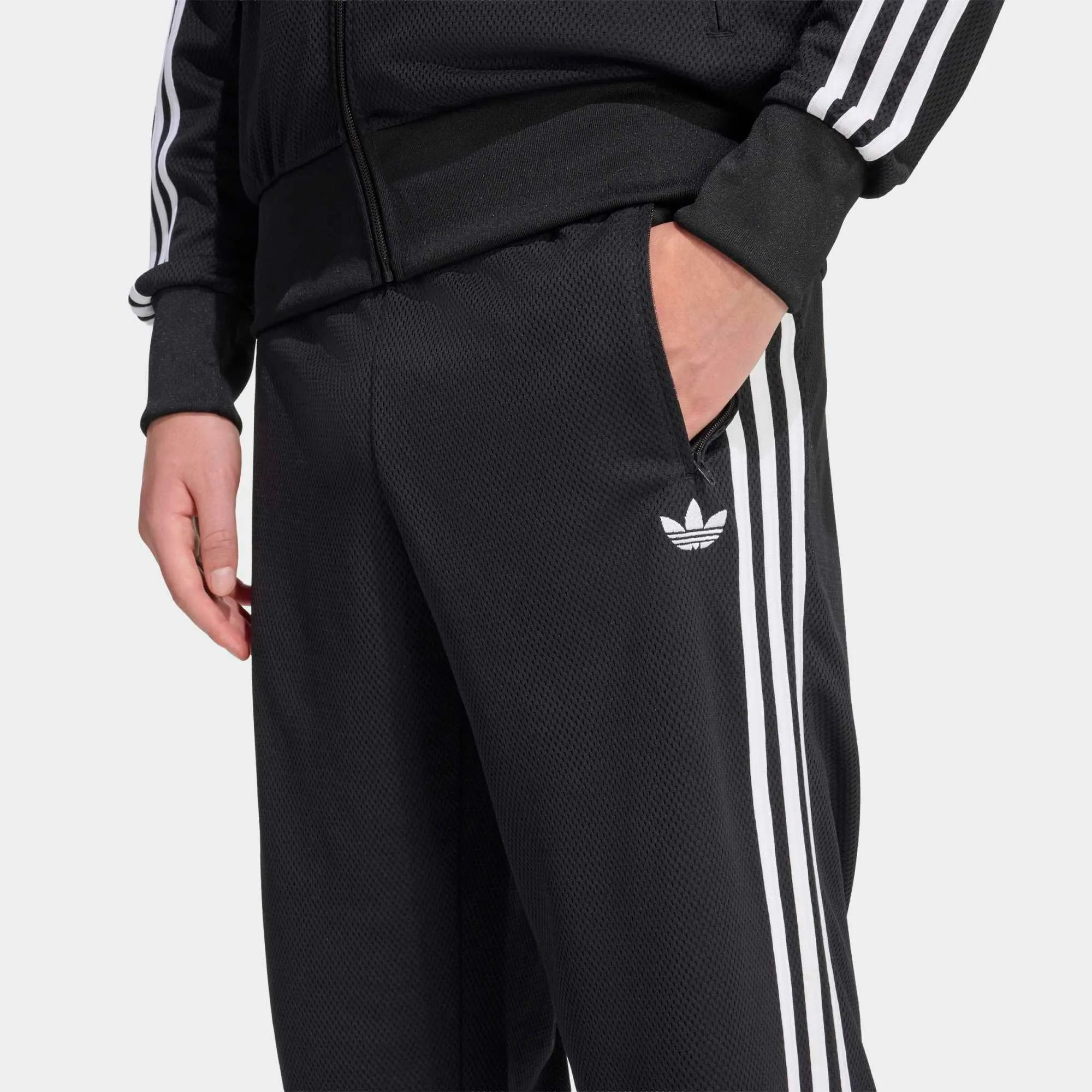 “Adidas Originals Firebird Track Pants Mesh in Schwarz mit weißen Streifen, Frontansicht des Trefoil-Logos und Mesh-Textur bei Stickabush Berlin.“