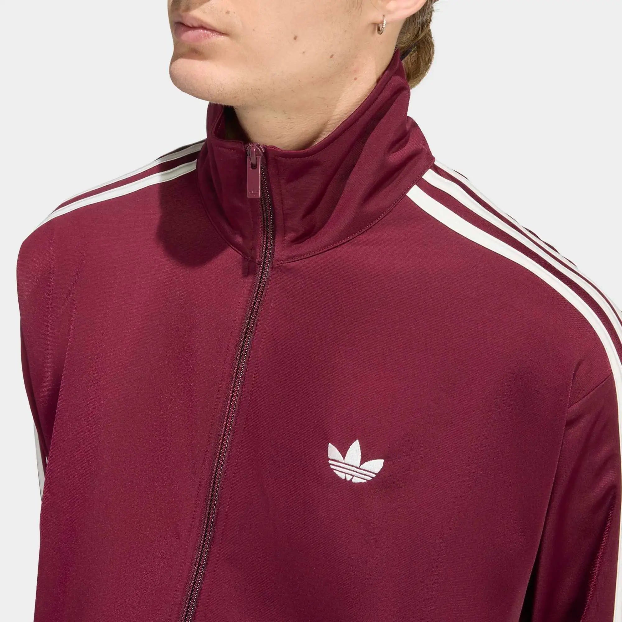 „Weinrote adidas Originals Firebird Trainingsjacke mit weißen 3-Streifen, Stehkragen und Trefoil-Logo in der Farbkombination Maroon / Off White bei Stickabush Berlin.“