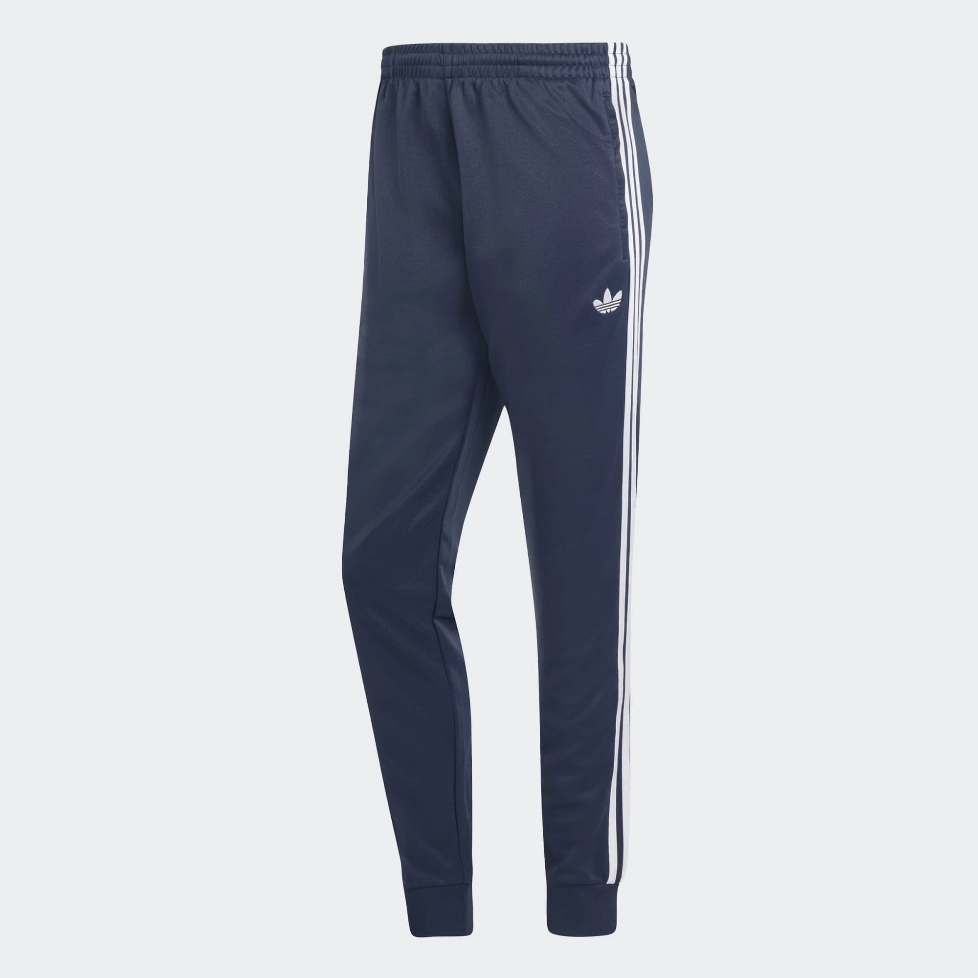 "Dunkelblaue adidas Originals SST Track Pant (Night Indigo) mit weißen 3-Streifen, Trefoil-Stickerei und Reißverschlusstaschen bei Stickabush Berlin."